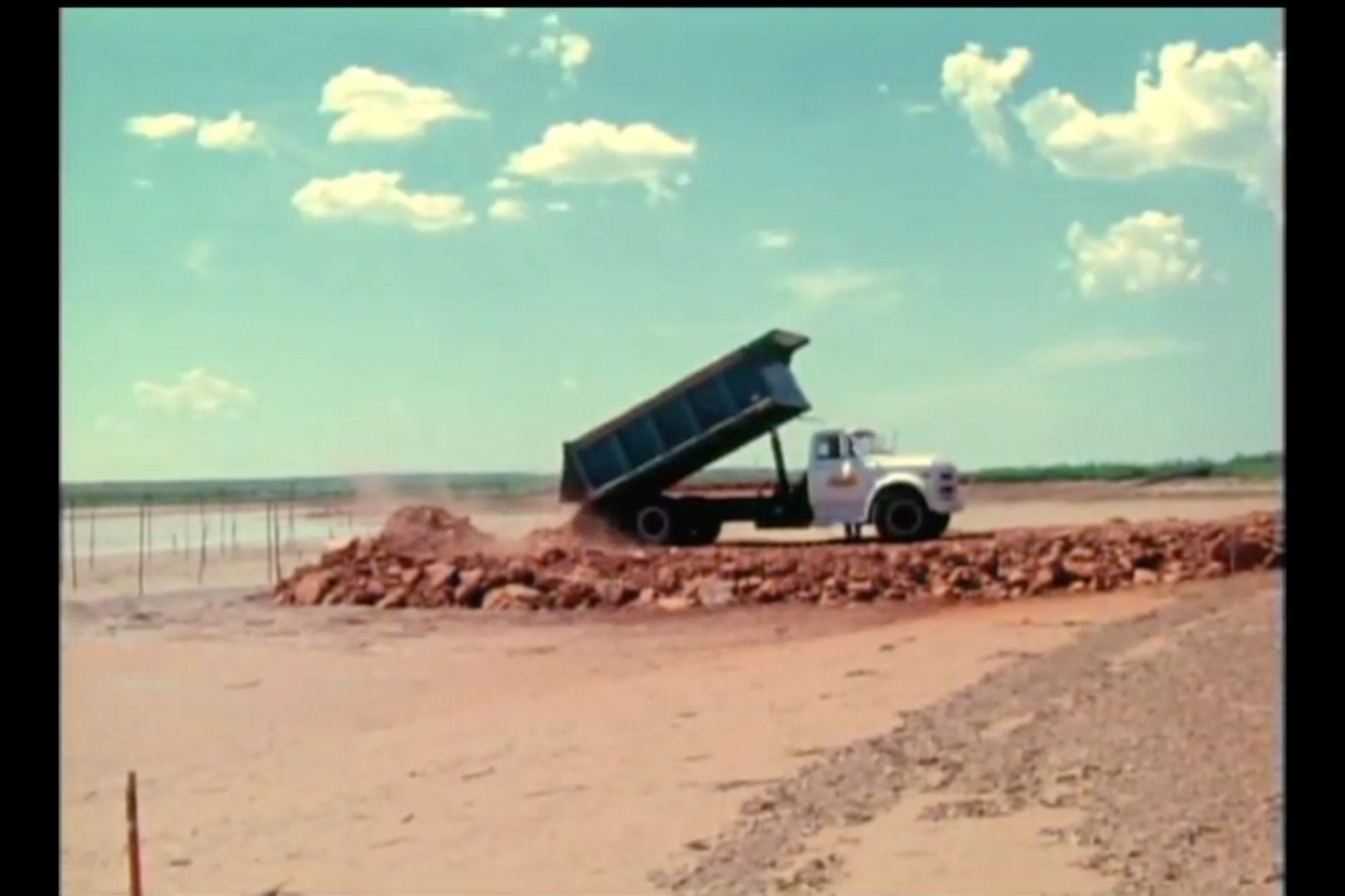 A dump truck dumping rock and earth at the edge of a lakebed