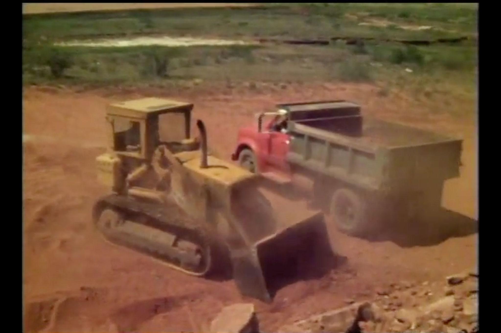 A yellow front loader and a red dump truck driving past each other
