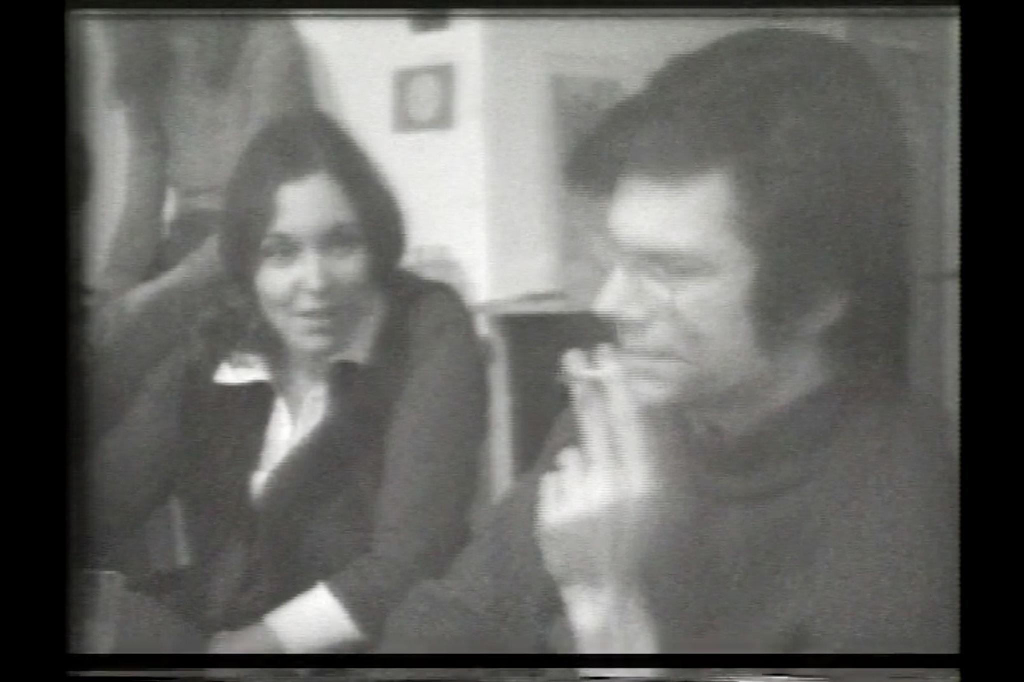 Black and white, a young woman and man seated next to each other in conversation.