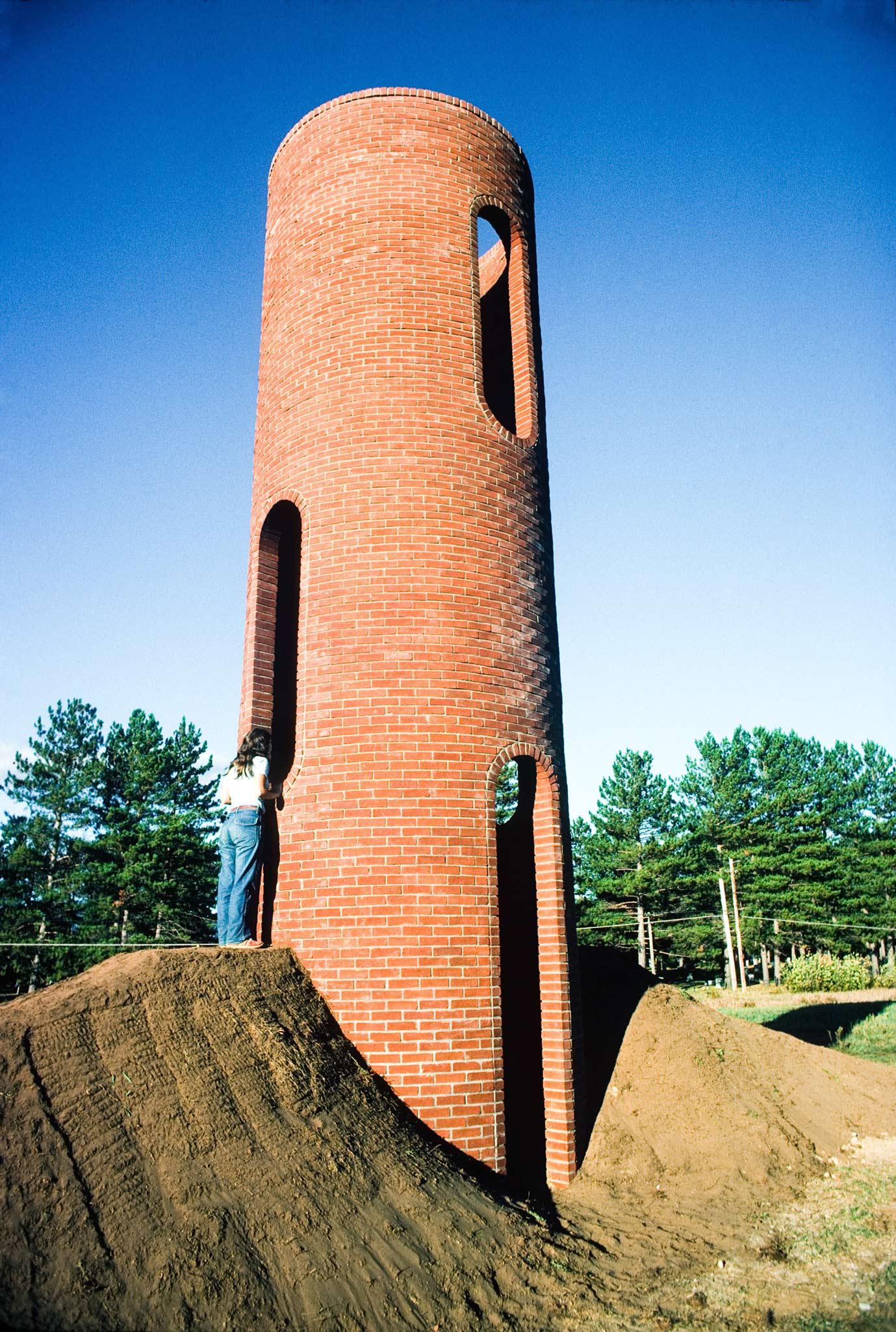 a figure peering into a window of a tall circular brick structure with round arched windows