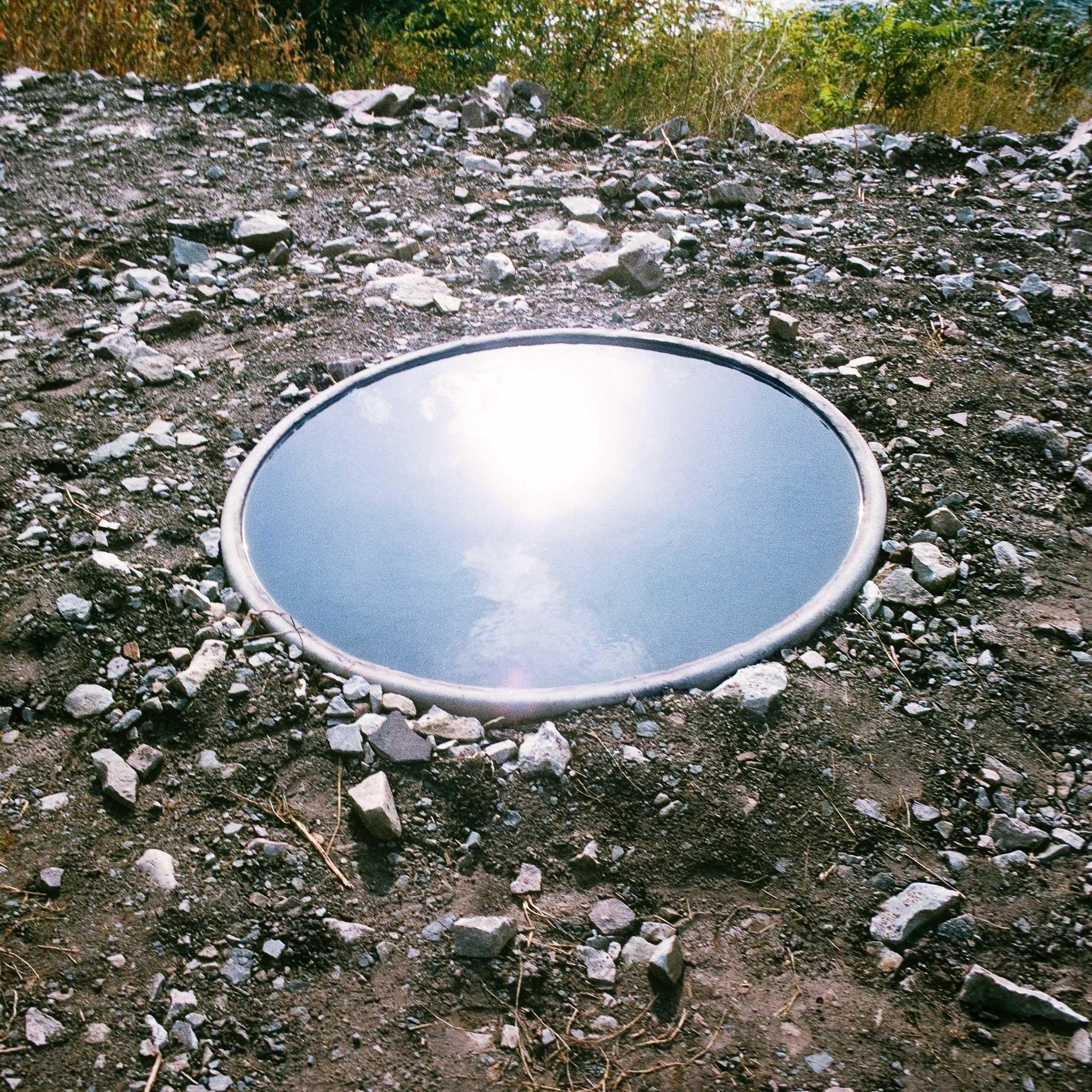 A circular pool of water reflecting a blue sky.
