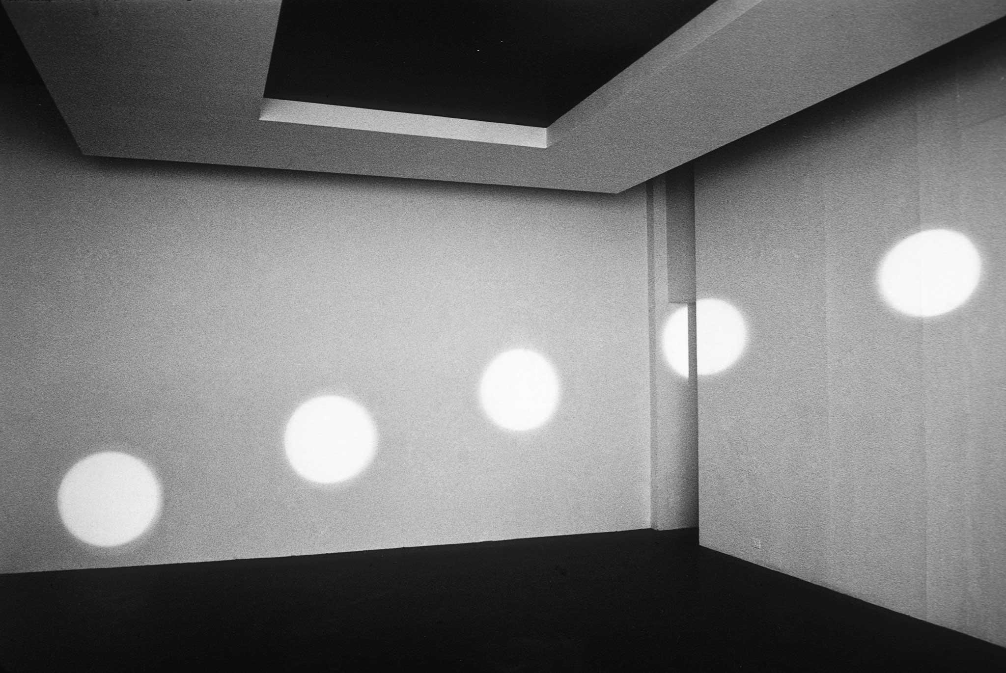 circular orbs of light reflected on two white walls of a room with no windows