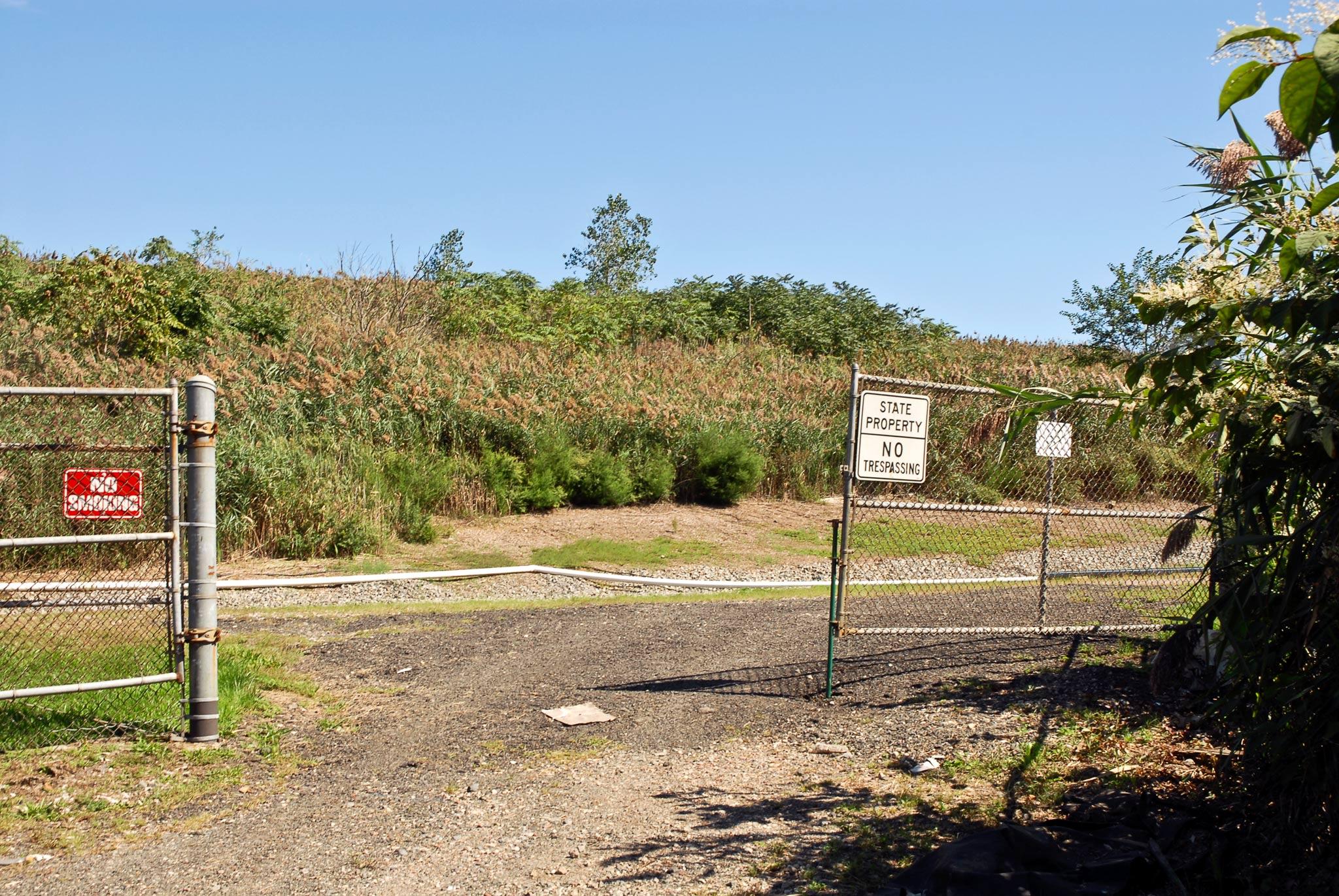 An entry gate on a gravel road with a vegetated landmass in the background
