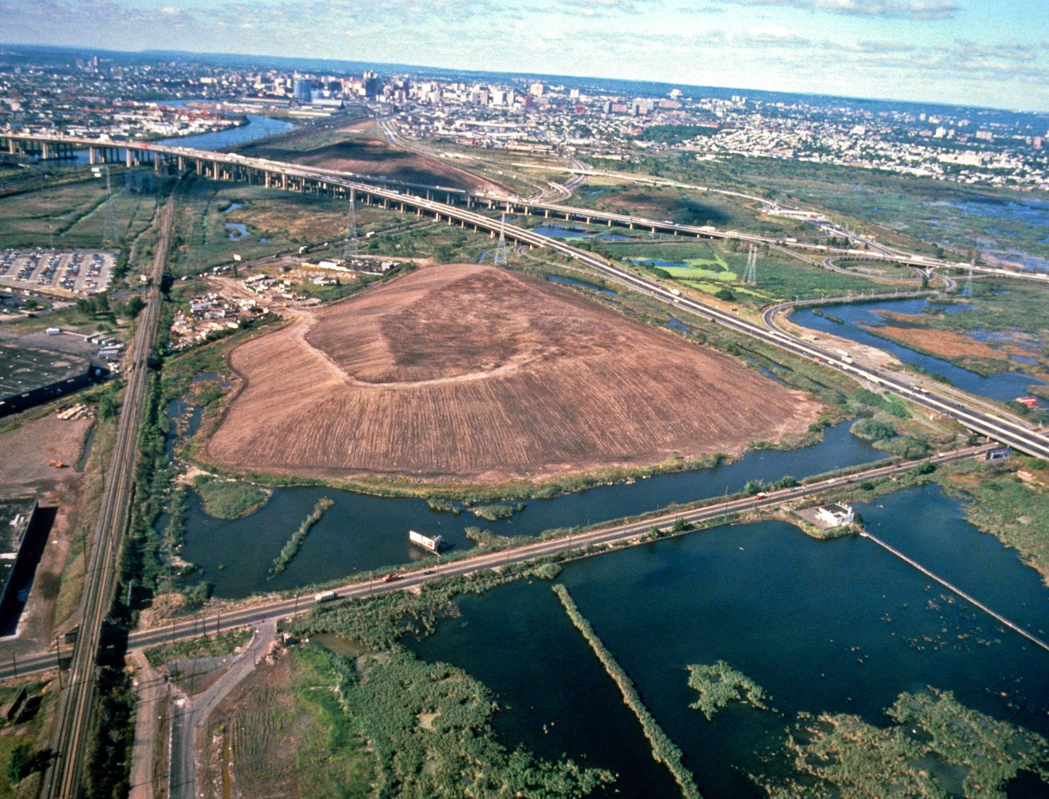 An aerial view of a triangular mounded landmass, surrounding by roads and rail tracks