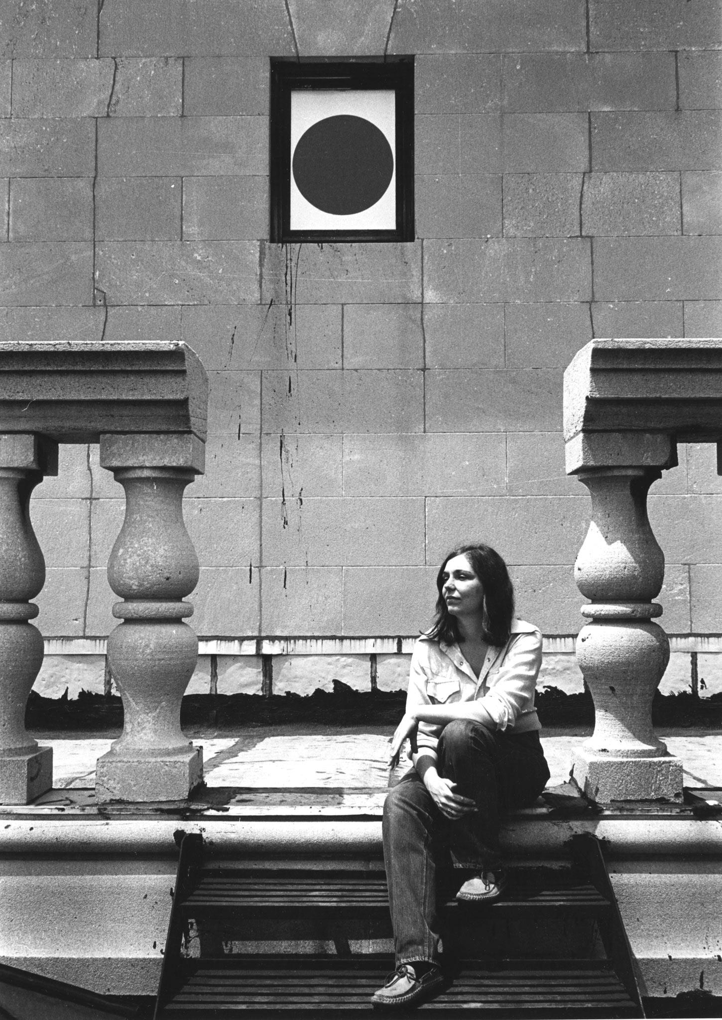 a person sits on stone steps with a large railing and a circular window inside a rectangular opening is behind them.