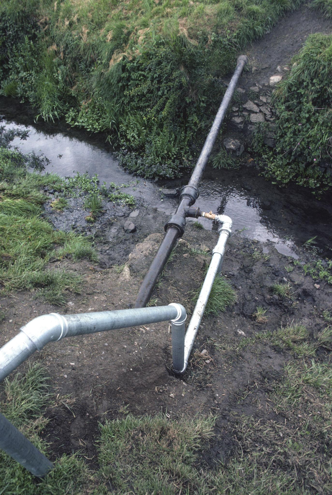 galvanized steel pipes flowing downhill and tying into larger pipes in a muddy ditch