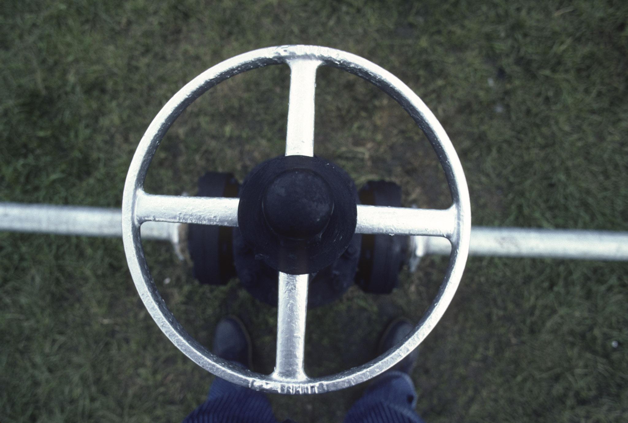 looking down on a galvanized steel valve with a persons shoes visible beneath it