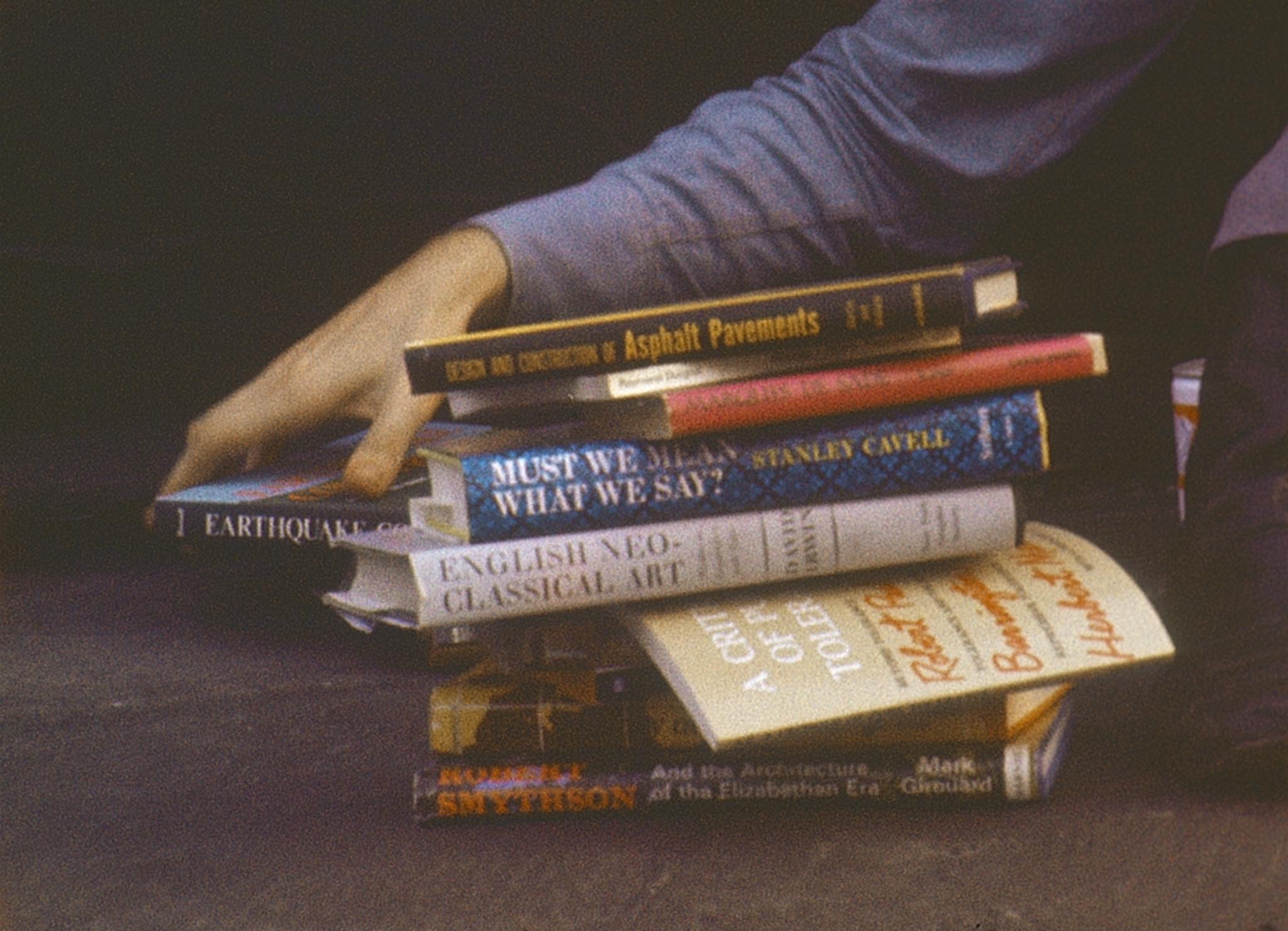 a pile of books with an arm reaching down to grab one