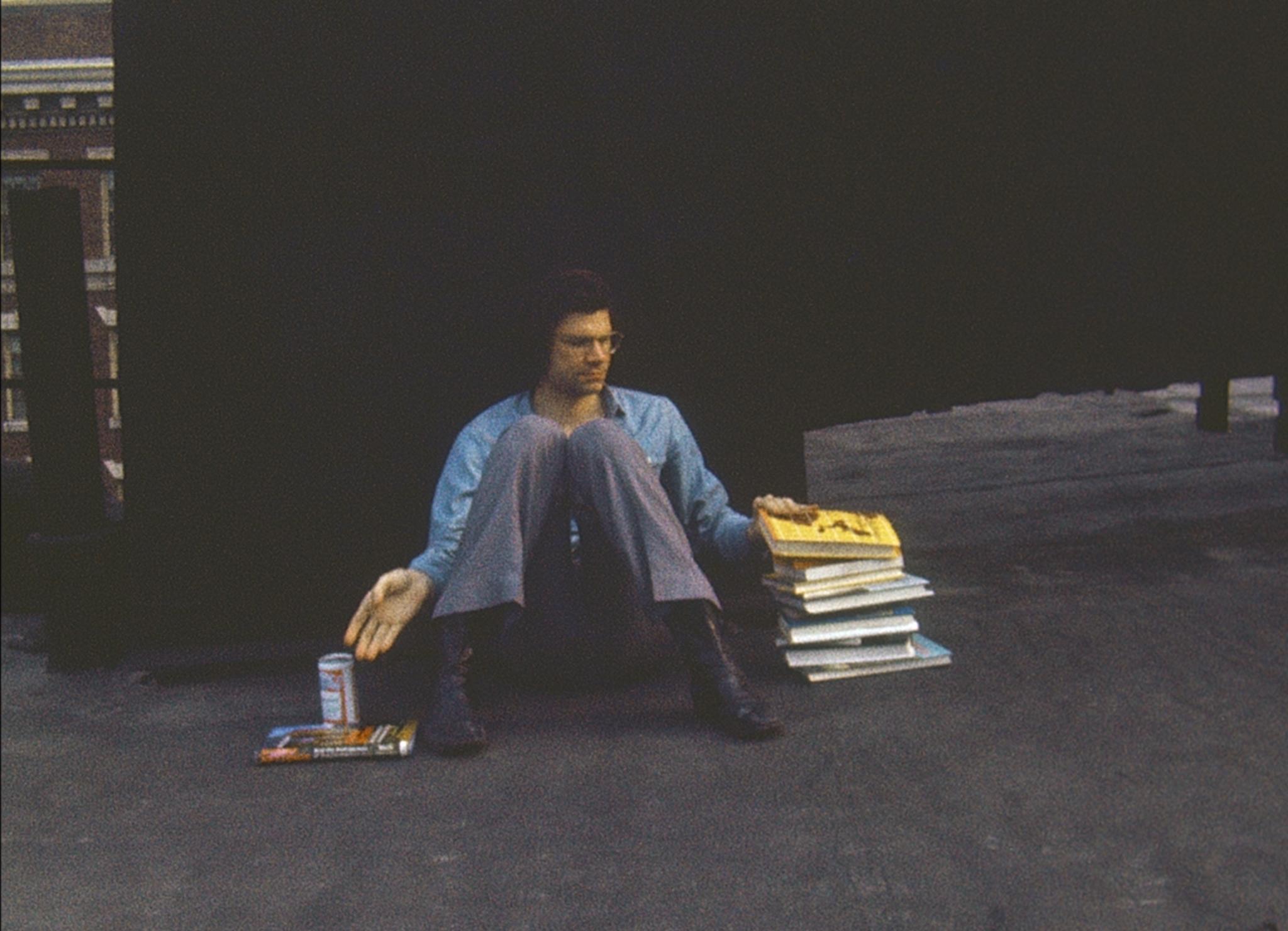 person sitting on the ground on a rooftop with a large pile of books beside them