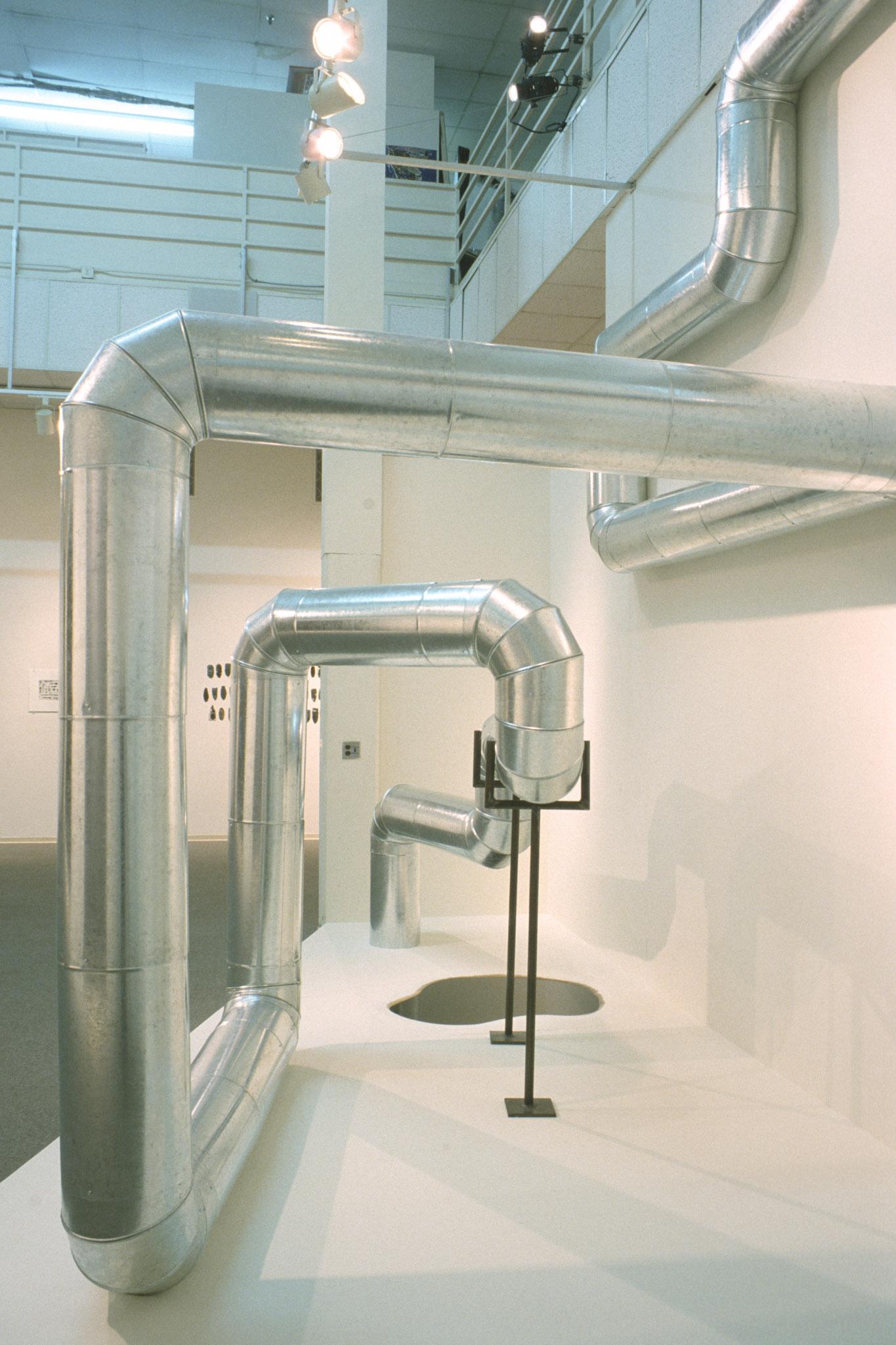 large steel duct zig zags through the air and along a wall in a gallery space.