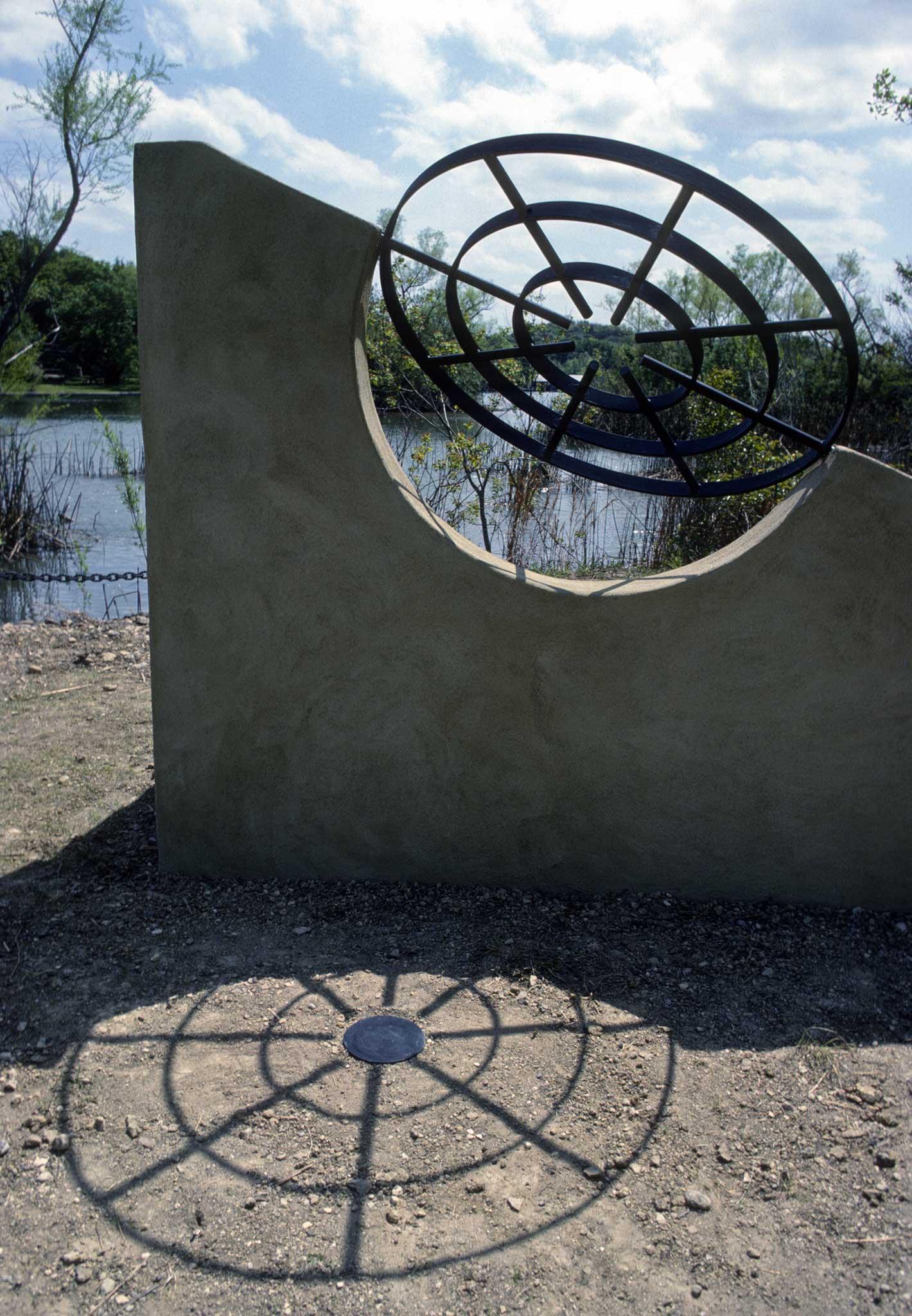 a short undulating stucco wall with two round metal grates incorporated into the structure built on a lush lake shoreline