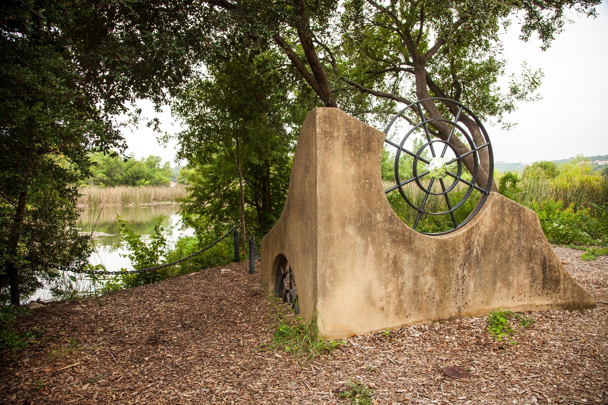 a short undulating stucco wall with two round metal grates incorporated into the structure built on a lush lake shoreline