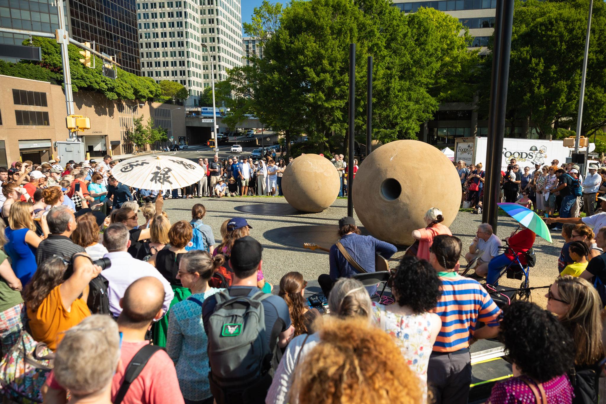 a large crowd gathered in an urban environment around two large concrete spheres