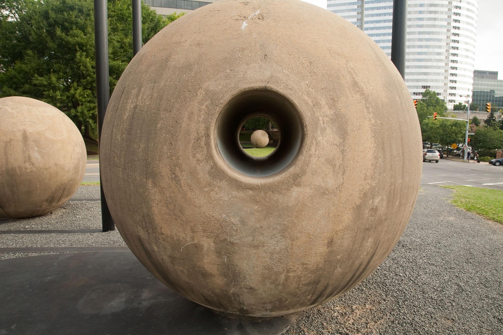 a large concrete sphere with a circular tunnel through the center that perfectly frames another concrete sphere in the distance