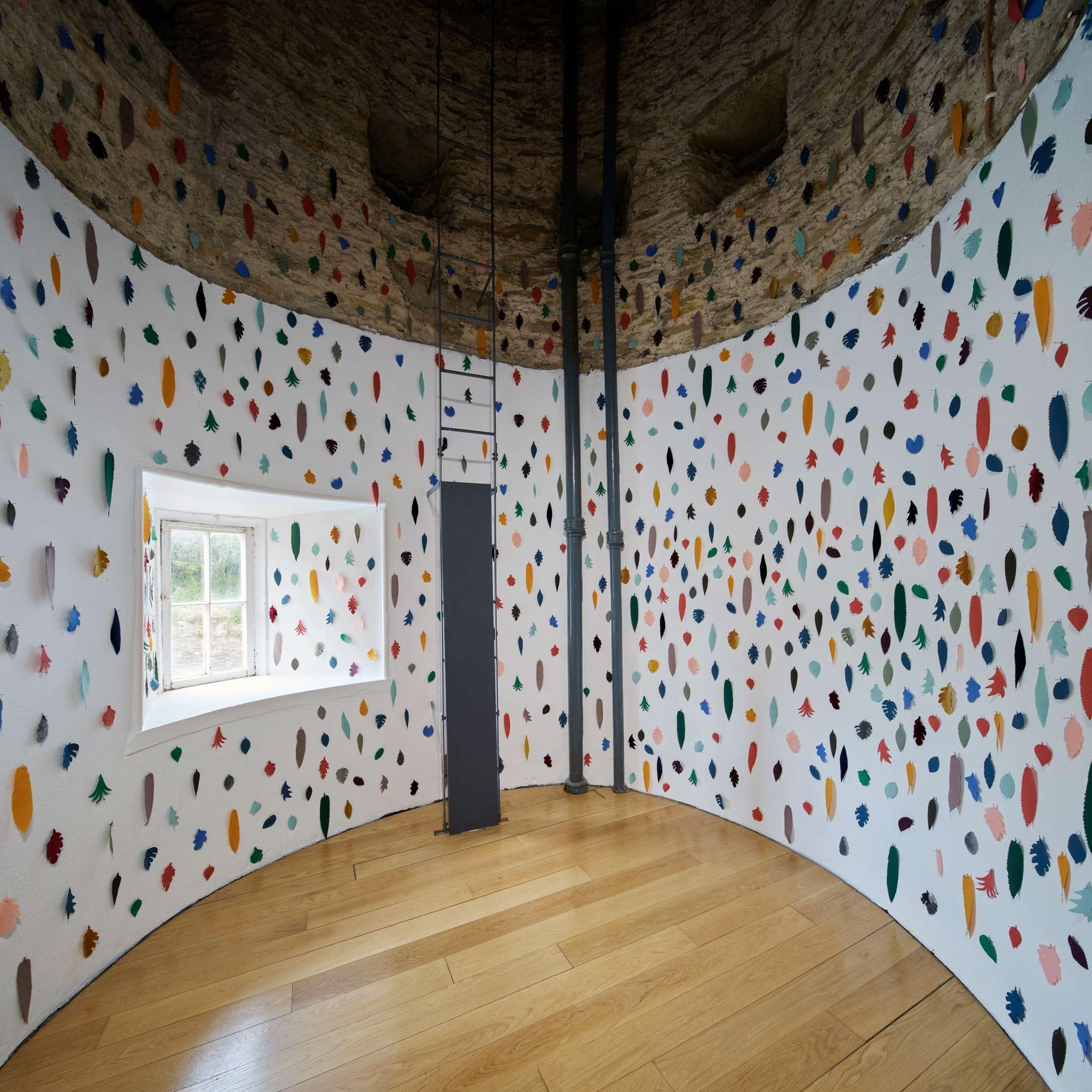 an installation of fabric leaves on white walls of a round room 