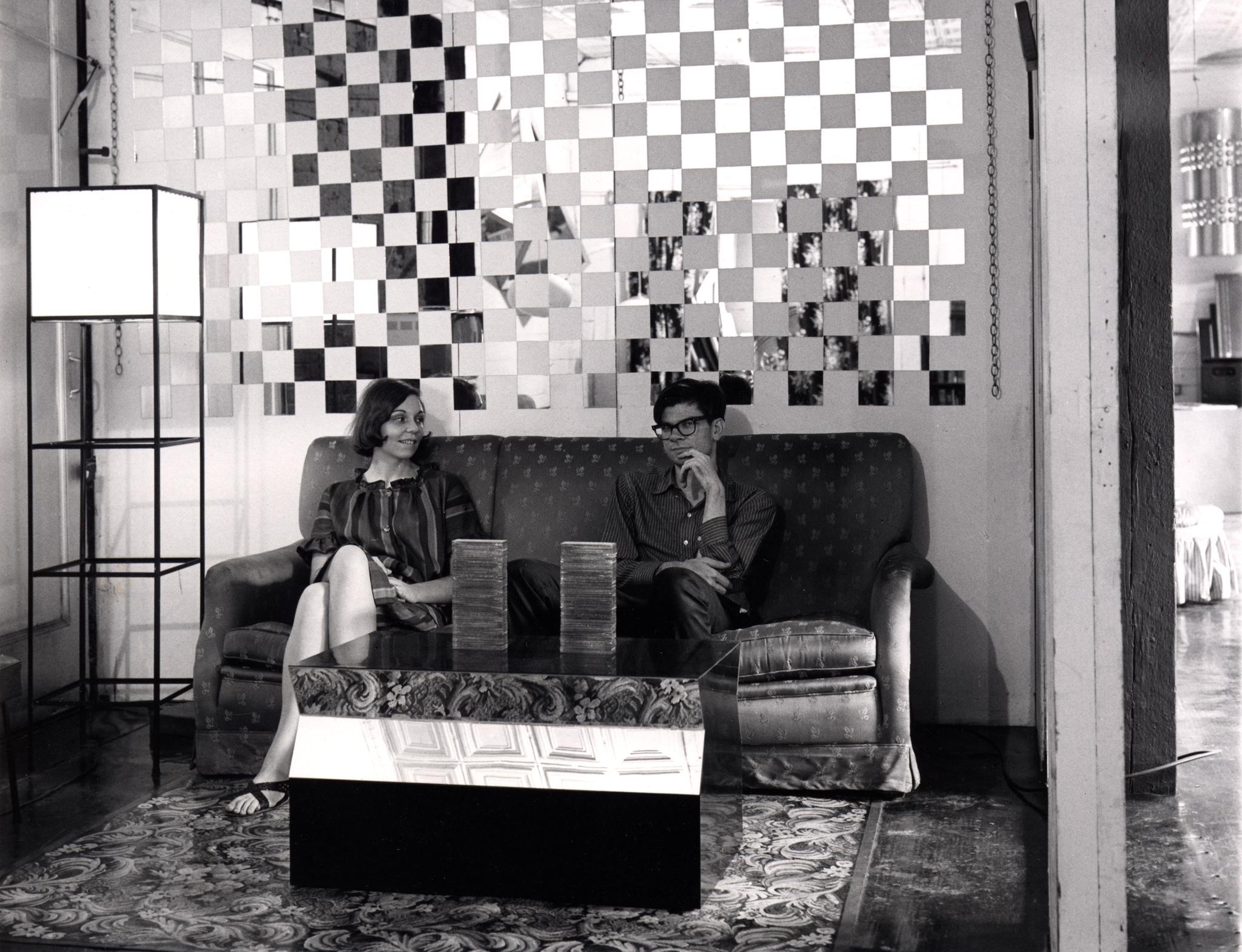 two people sitting on a couch with a mirrored wall behind them and a mirrored coffee table in front of them