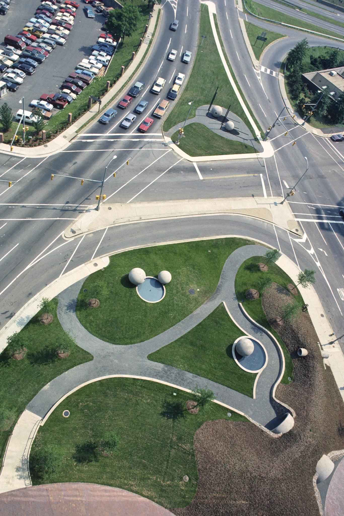 aerial view of a city park with concrete spheres, pools, and grass, surrounded by roadways