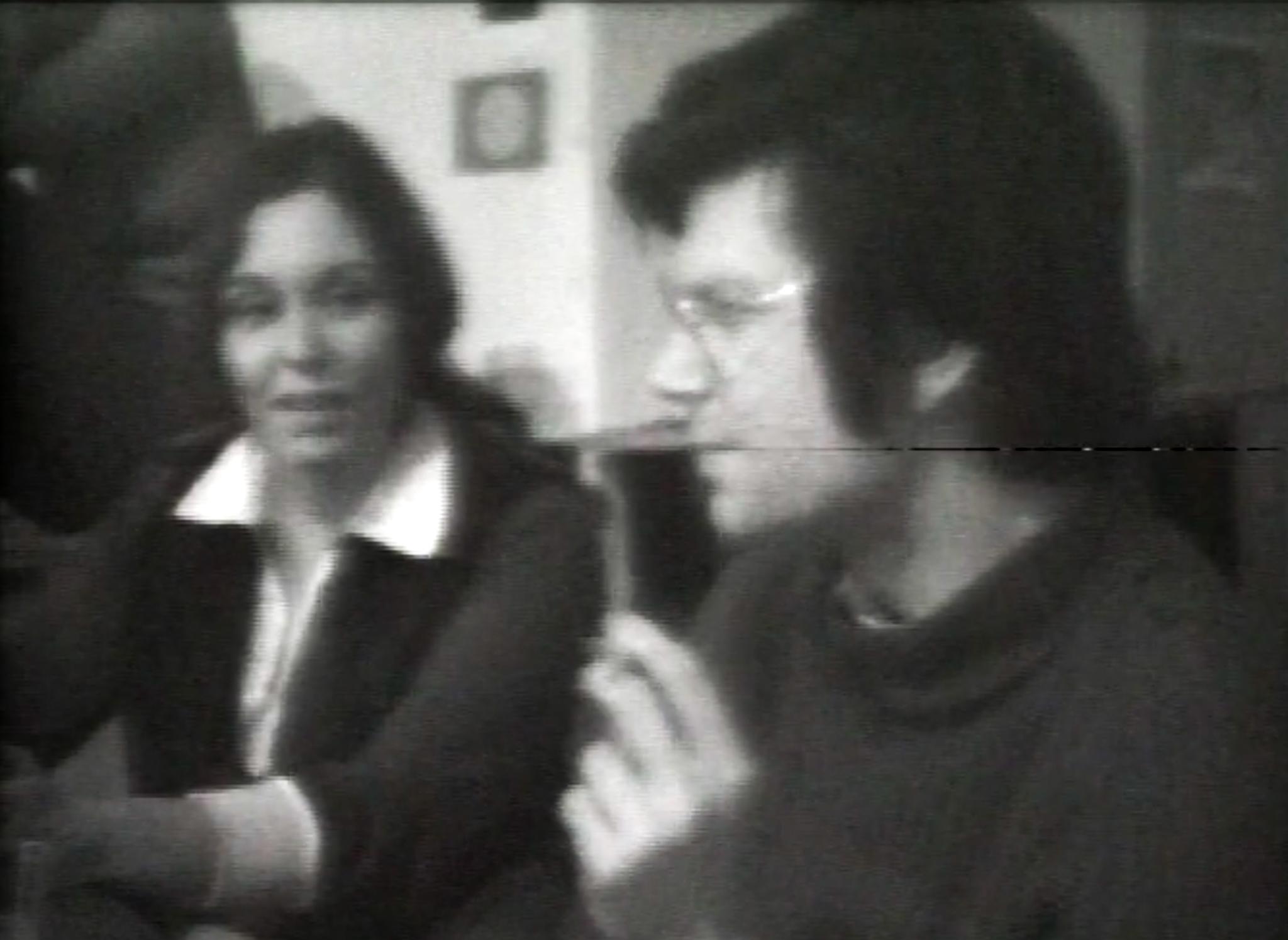 Black and white, a young woman and man seated next to each other in conversation.