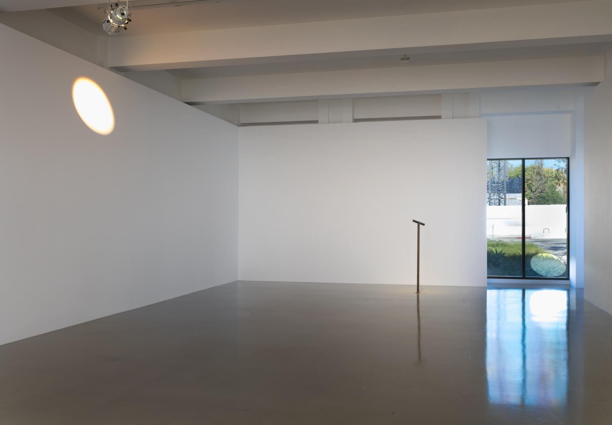 An exhibition space with a Locator in the center with an ellipse of light on one wall and a circular cutout over a window