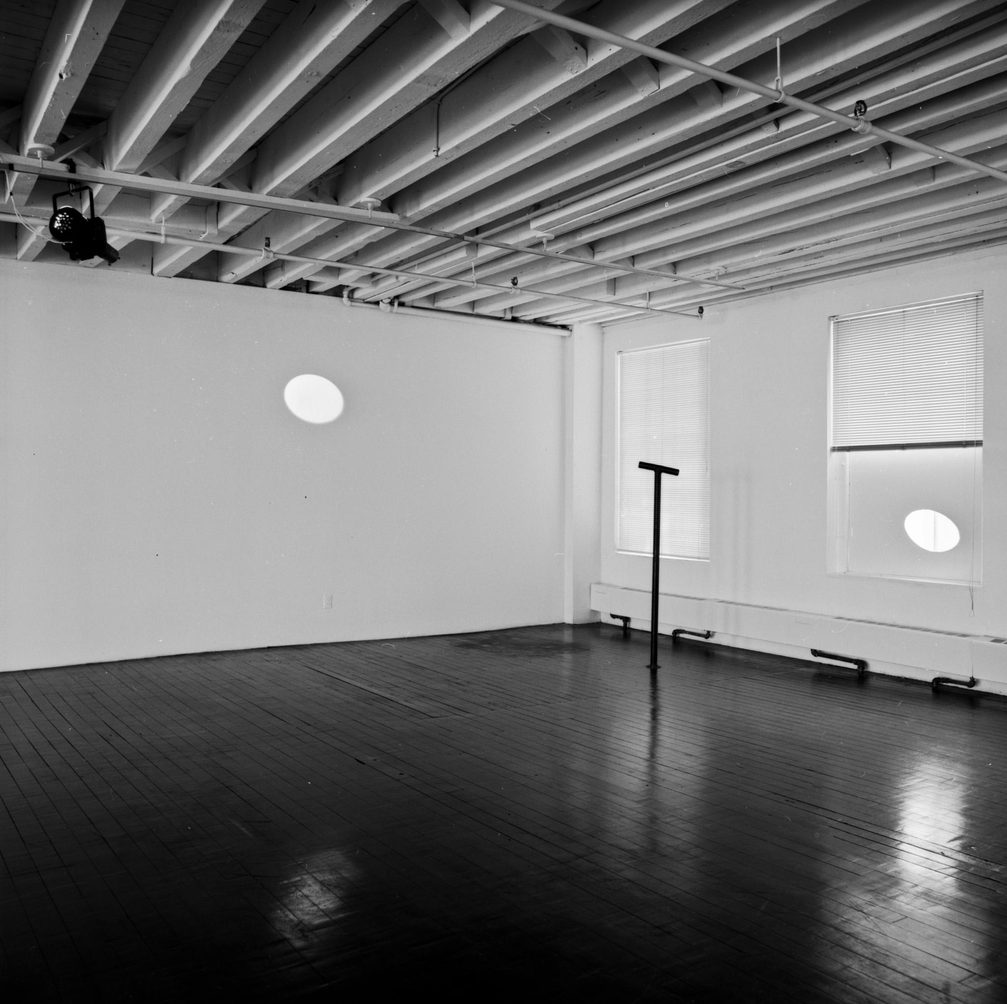 An exhibition space with a Locator in the center with an ellipse of light on one wall and a circular cutout over a window