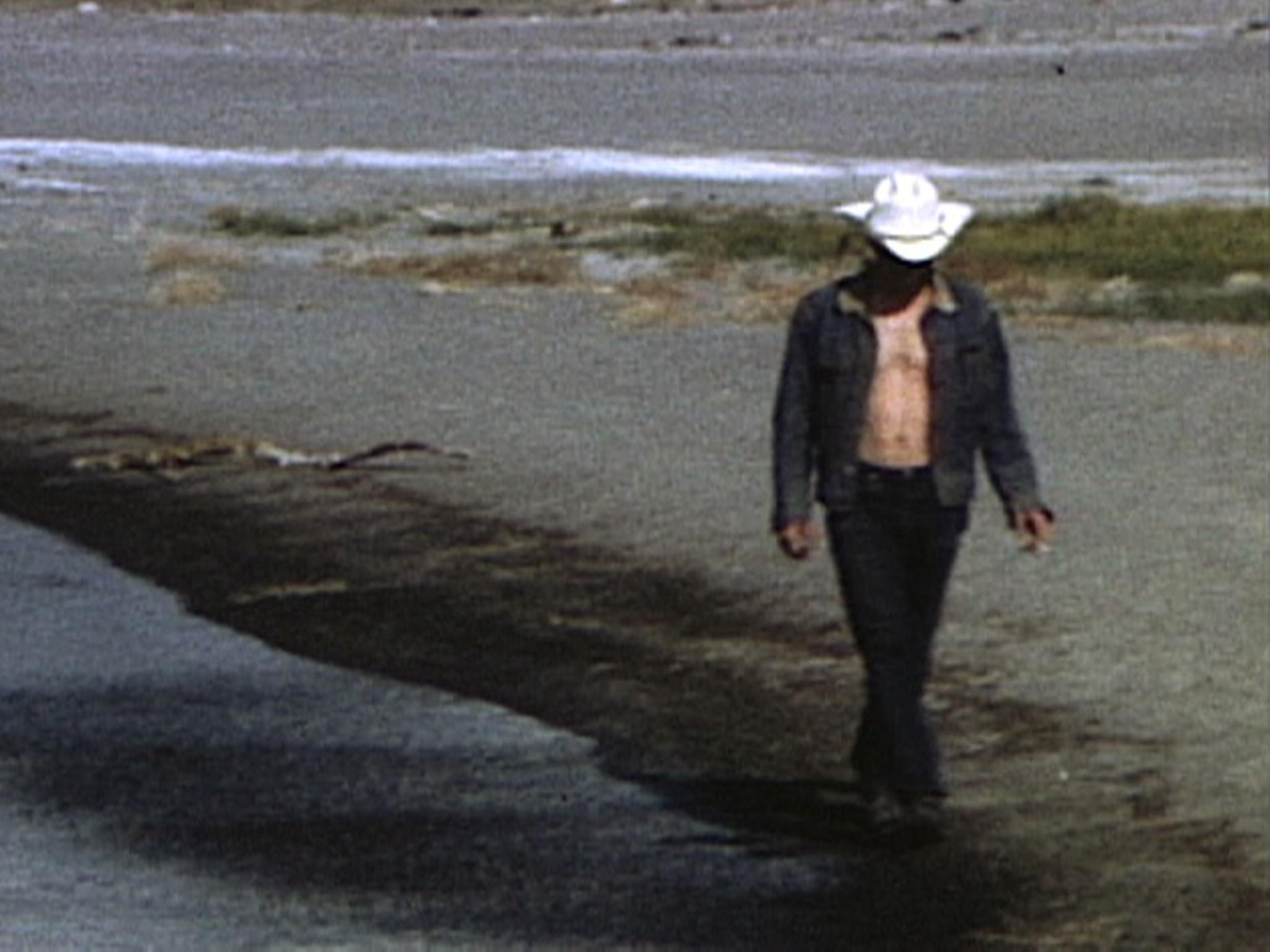 a man in a cowboy hat walks along a shore