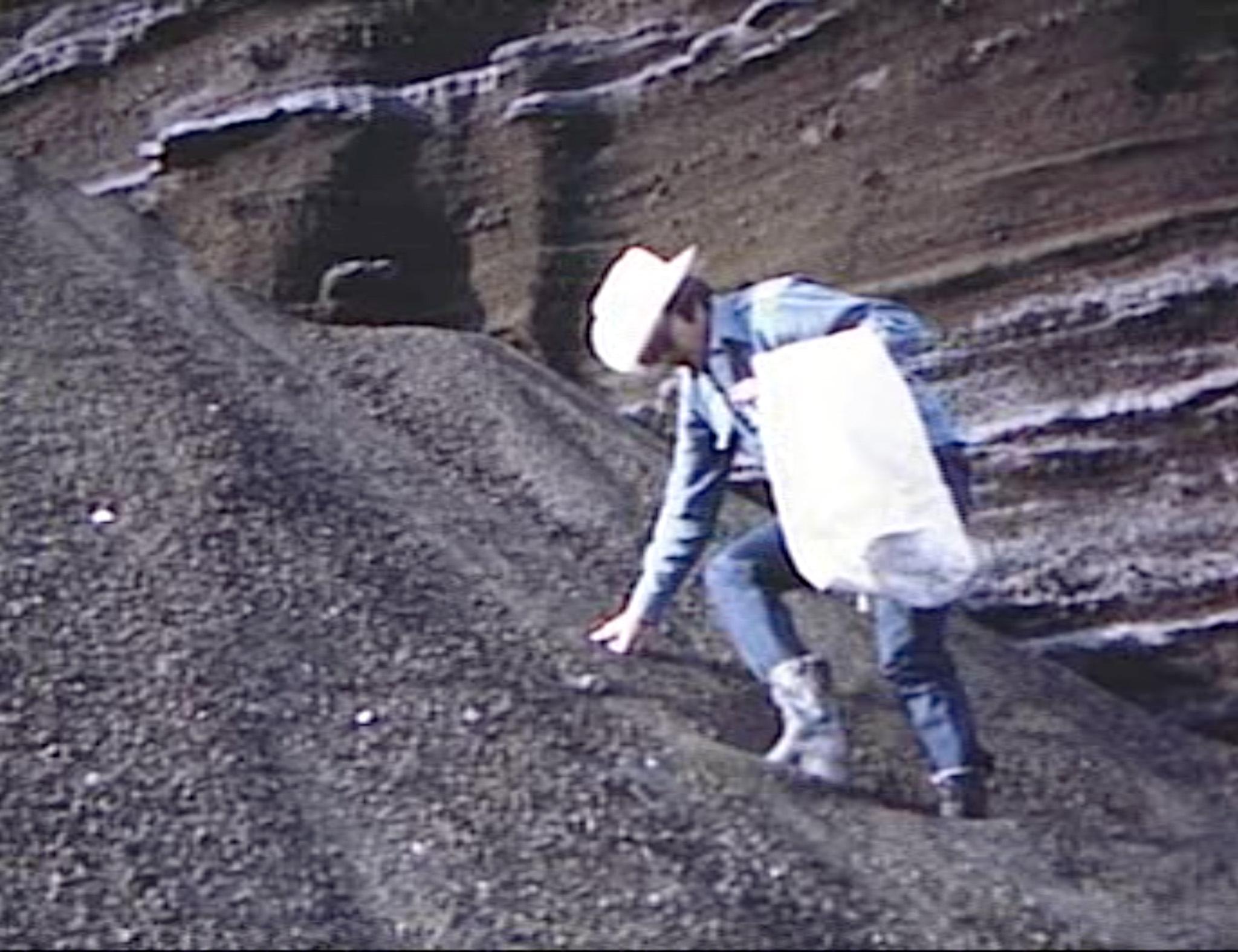 A man wearing a cowboy hat descending a steep slope of gravel