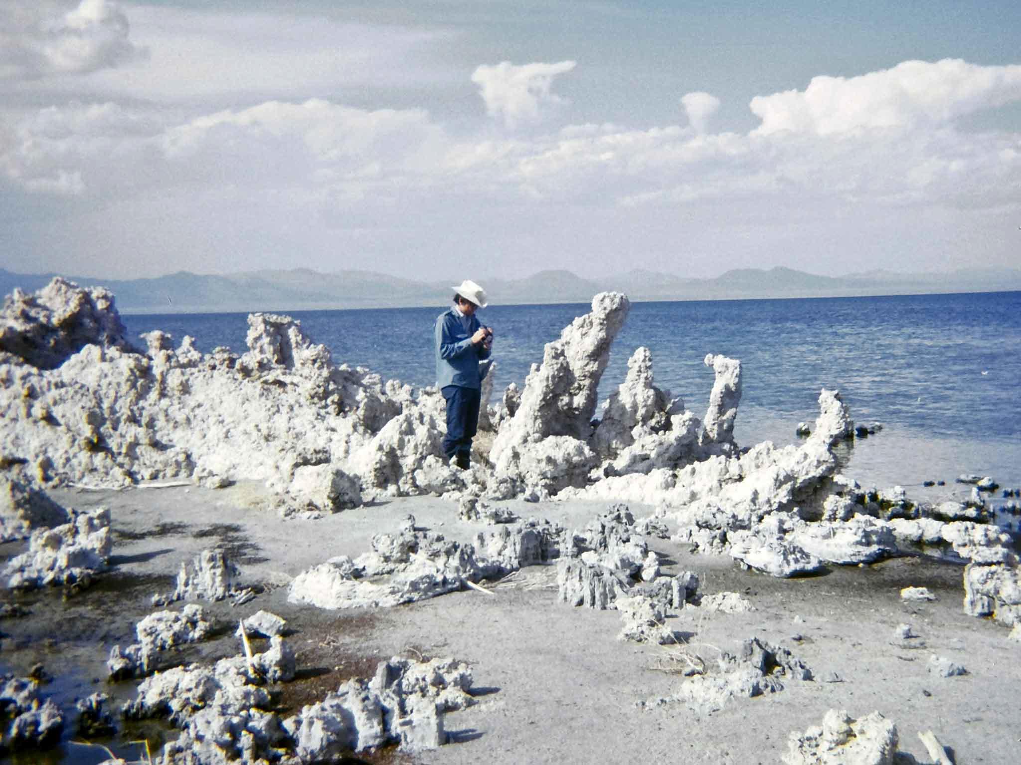 a man stands along a shoreline of a lake with unusual geology