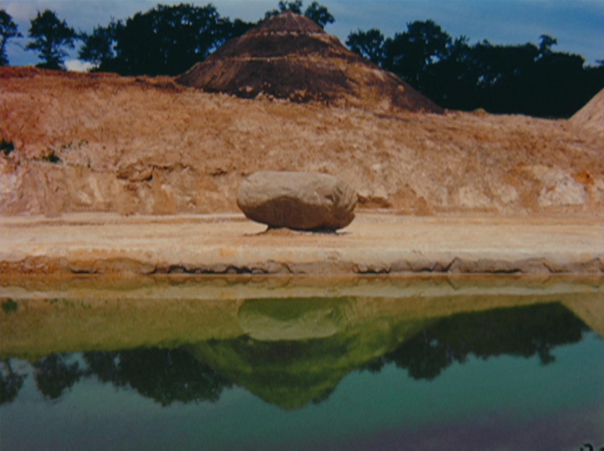 a large boulder on top of sand with a spiral hill in the background