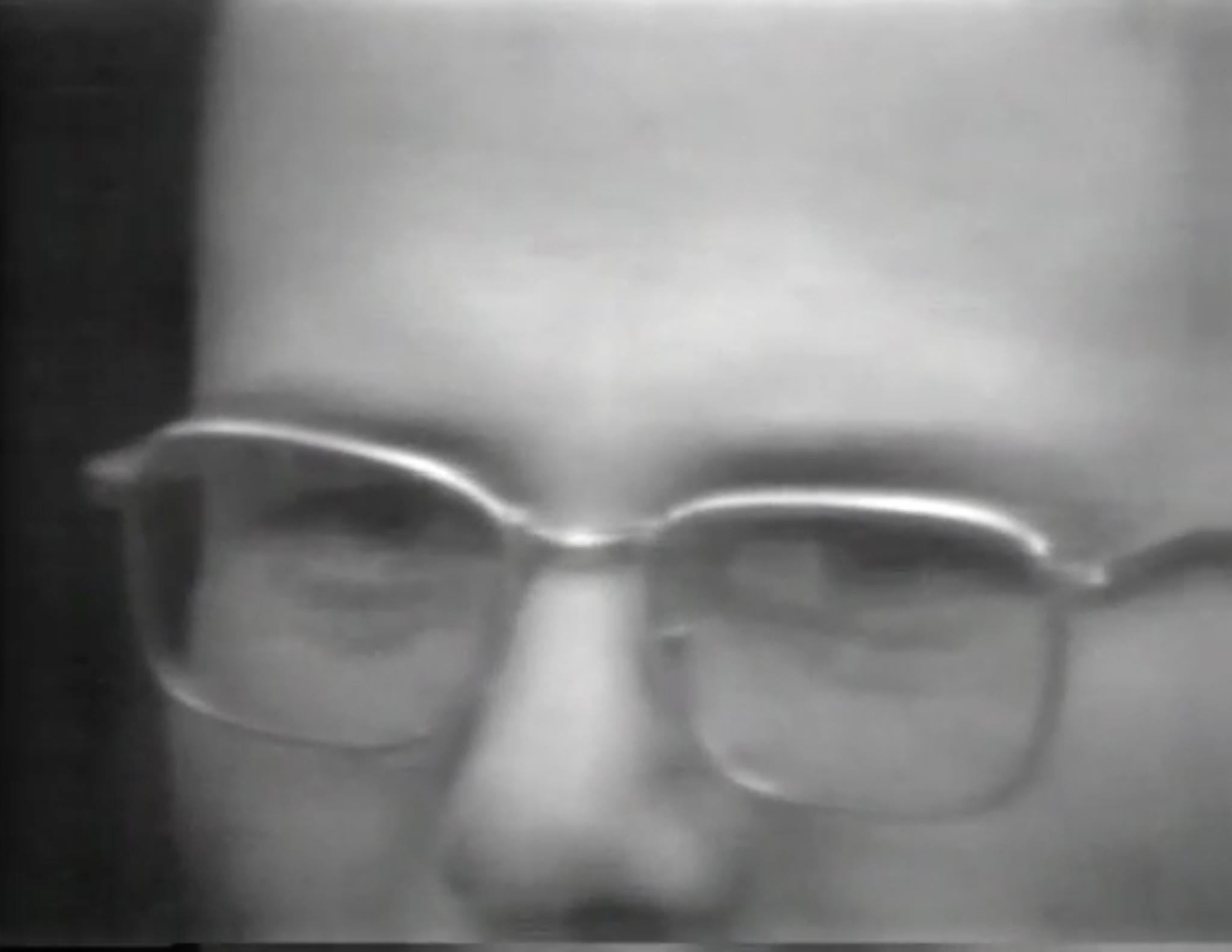 Black and white close-up image of a man with glasses.