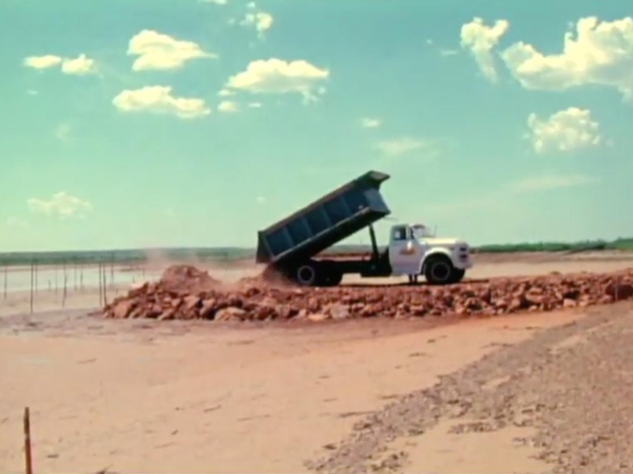 A dump truck dumping rock and earth at the edge of a lakebed
