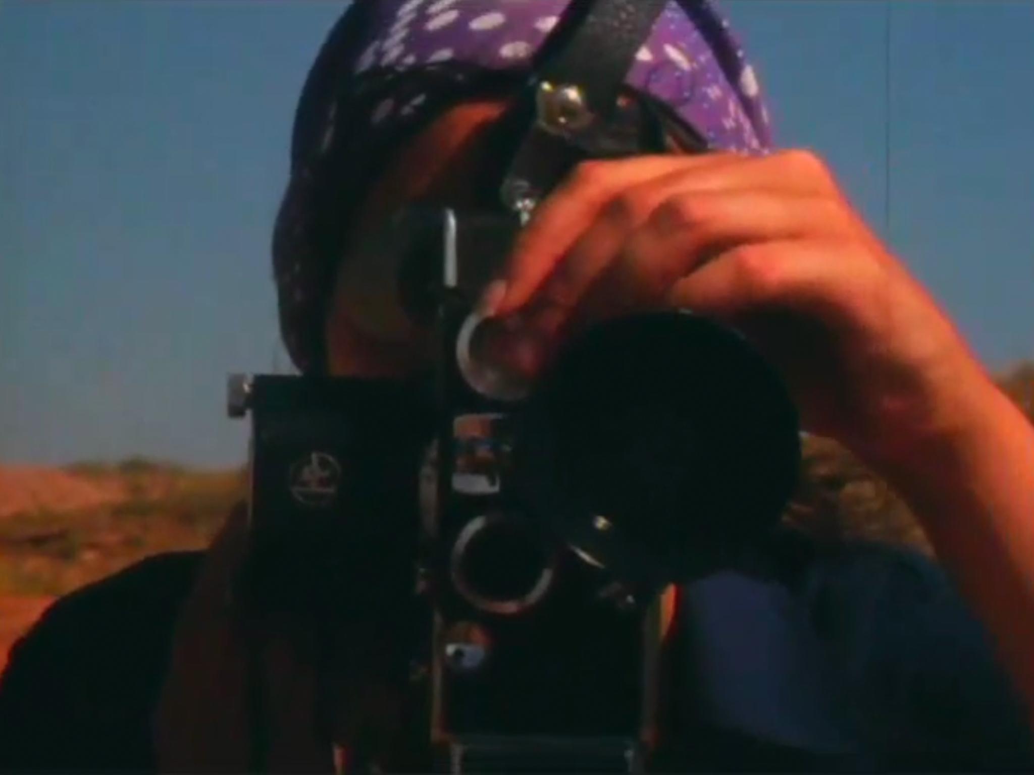 a close-up image of a person adjusting the focus on a film camera, which is pointed at the viewer.