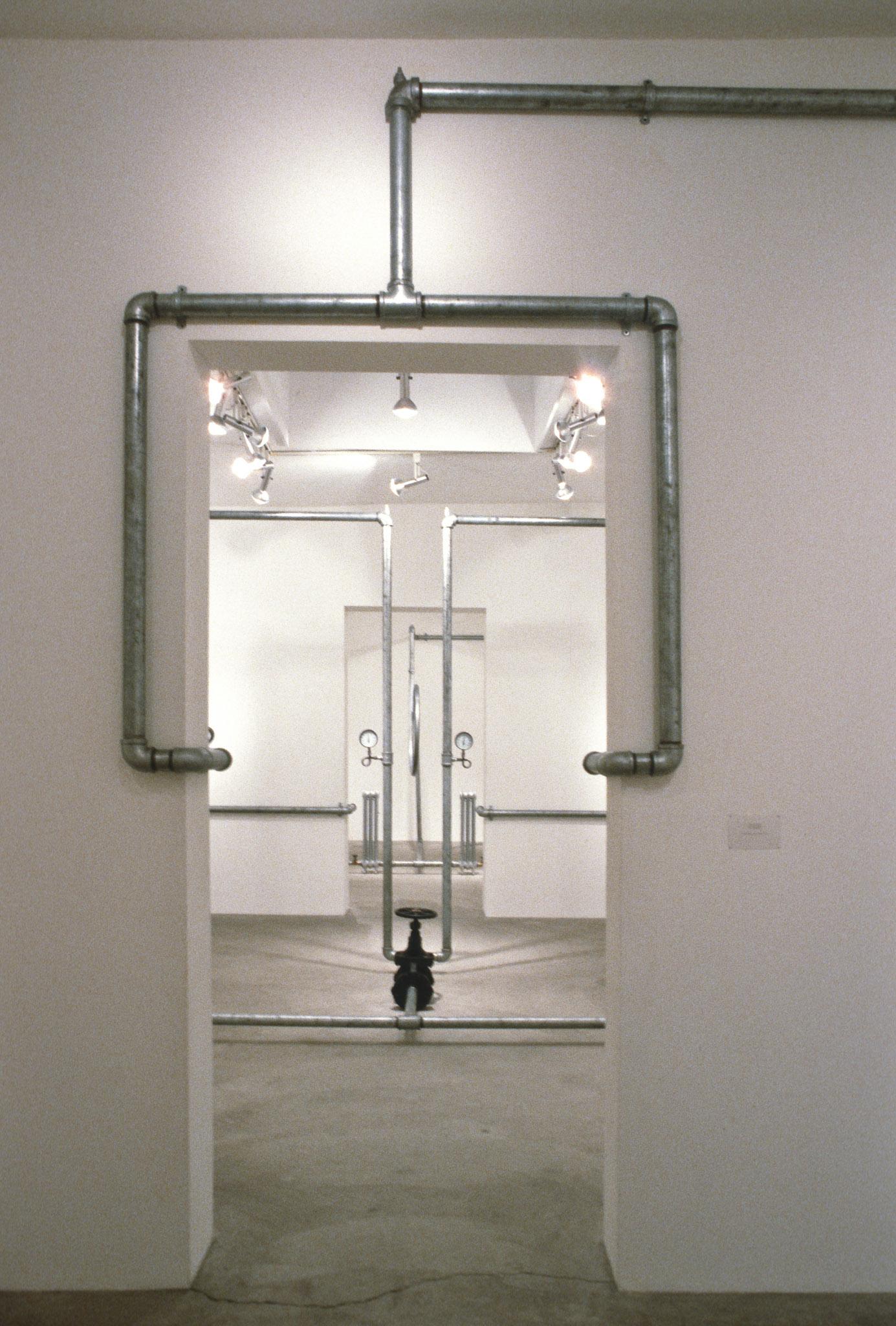 An installation of hot water pipes and gauges installed in a white walled gallery space