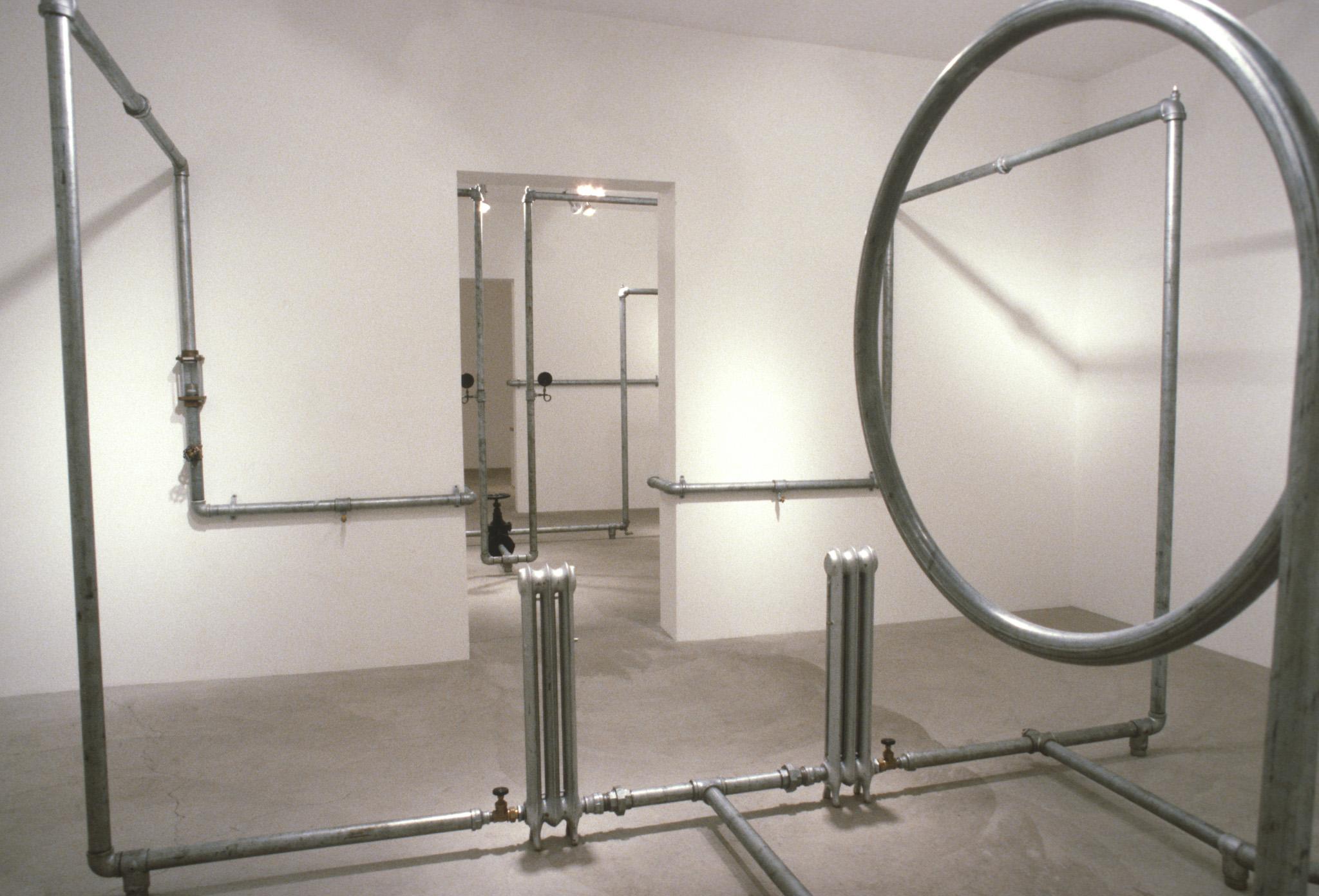 An installation of hot water pipes and gauges installed in a white walled gallery space