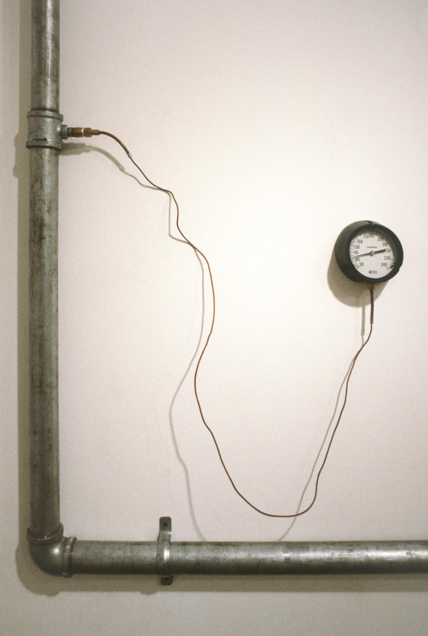 An installation of hot water pipes and gauges installed in a white walled gallery space
