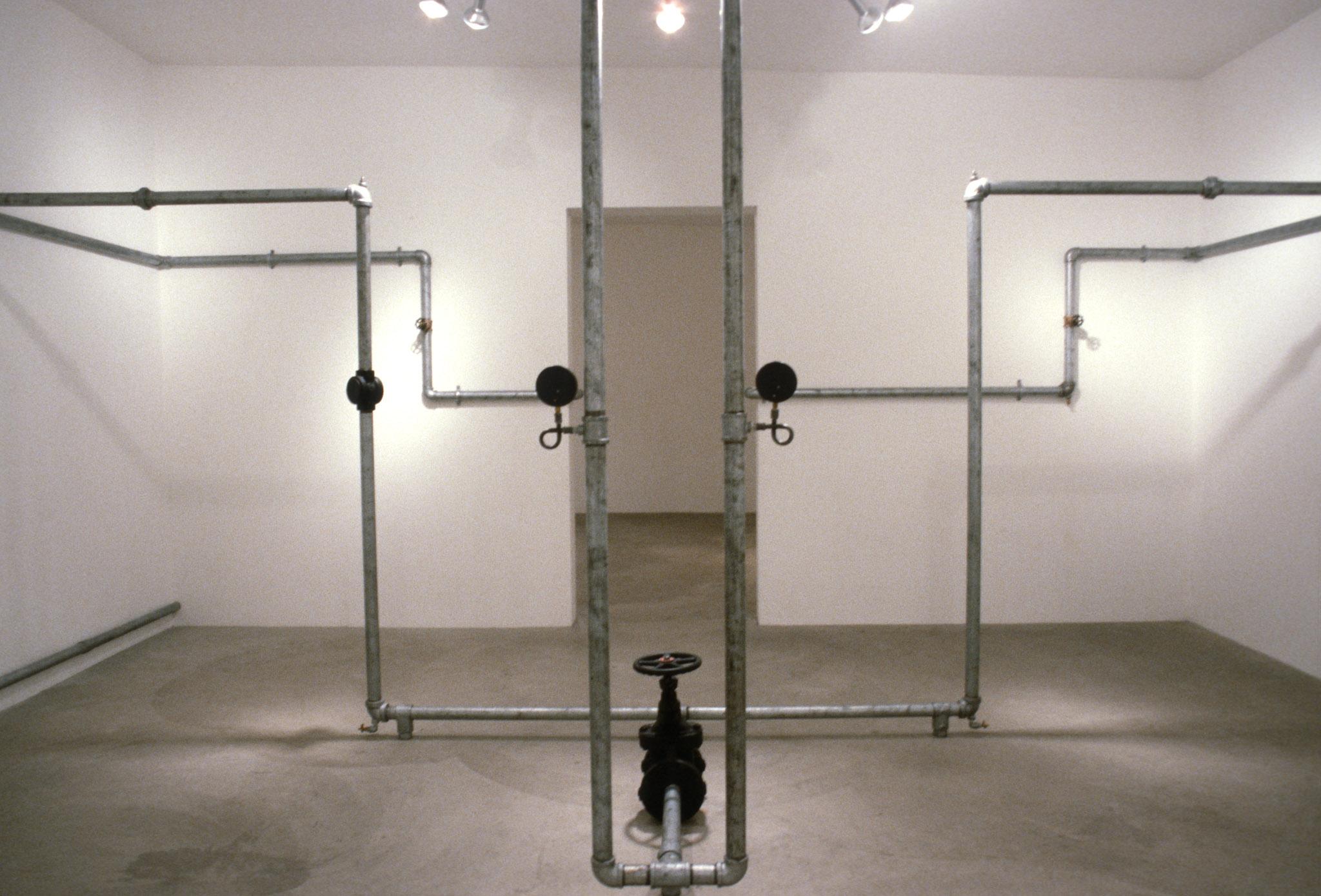 An installation of hot water pipes and gauges installed in a white walled gallery space