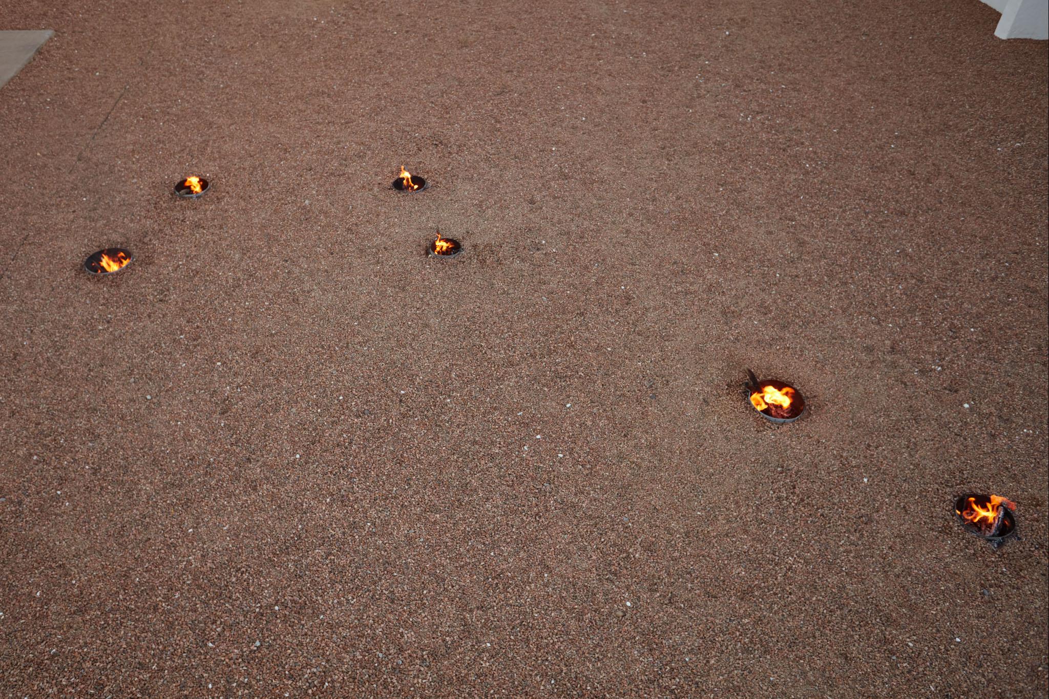 a courtyard with gravel and small firepits arranged in in the shape of the big dipper