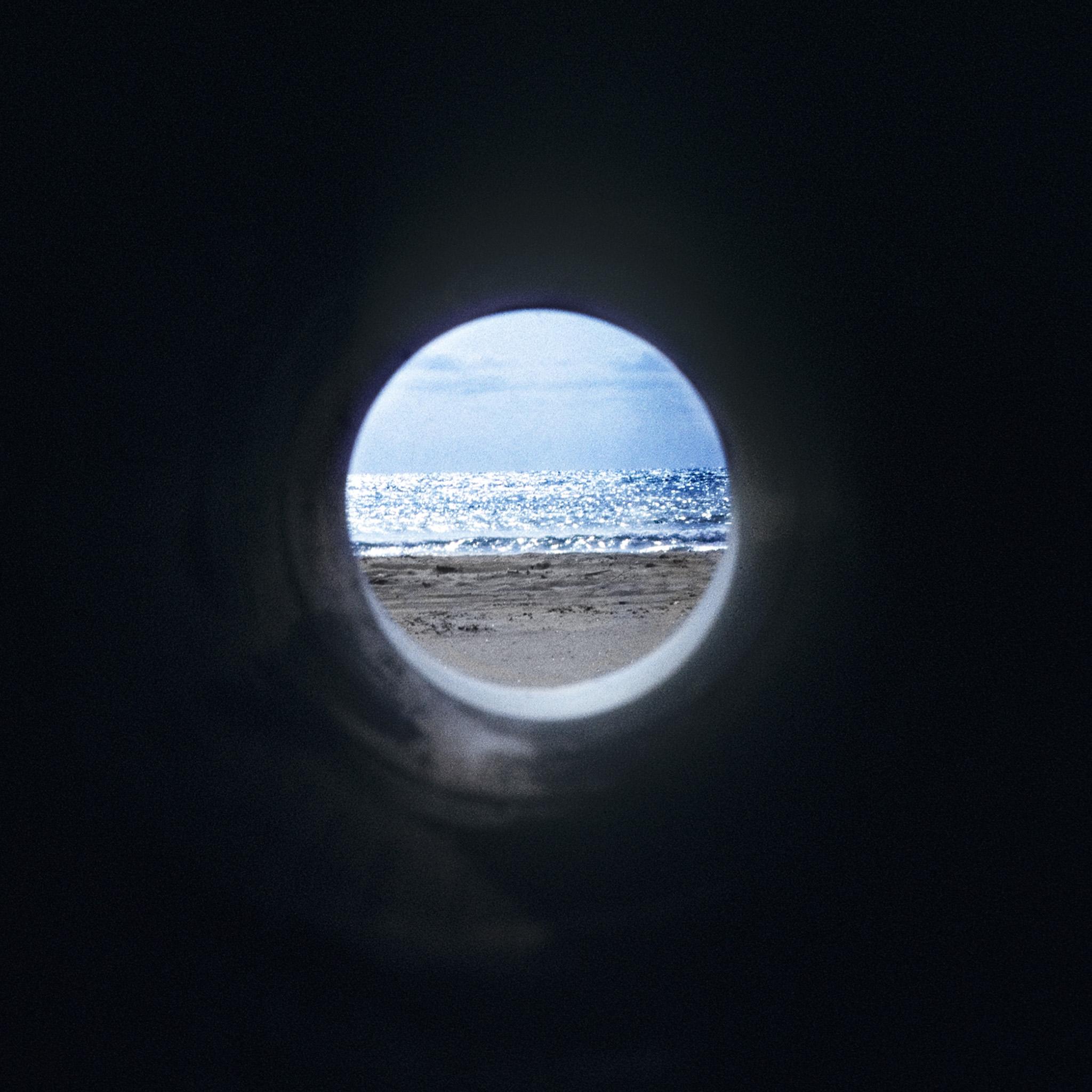 A circular pipe inserted through a sand dune framing a view of ocean and landscape horizons