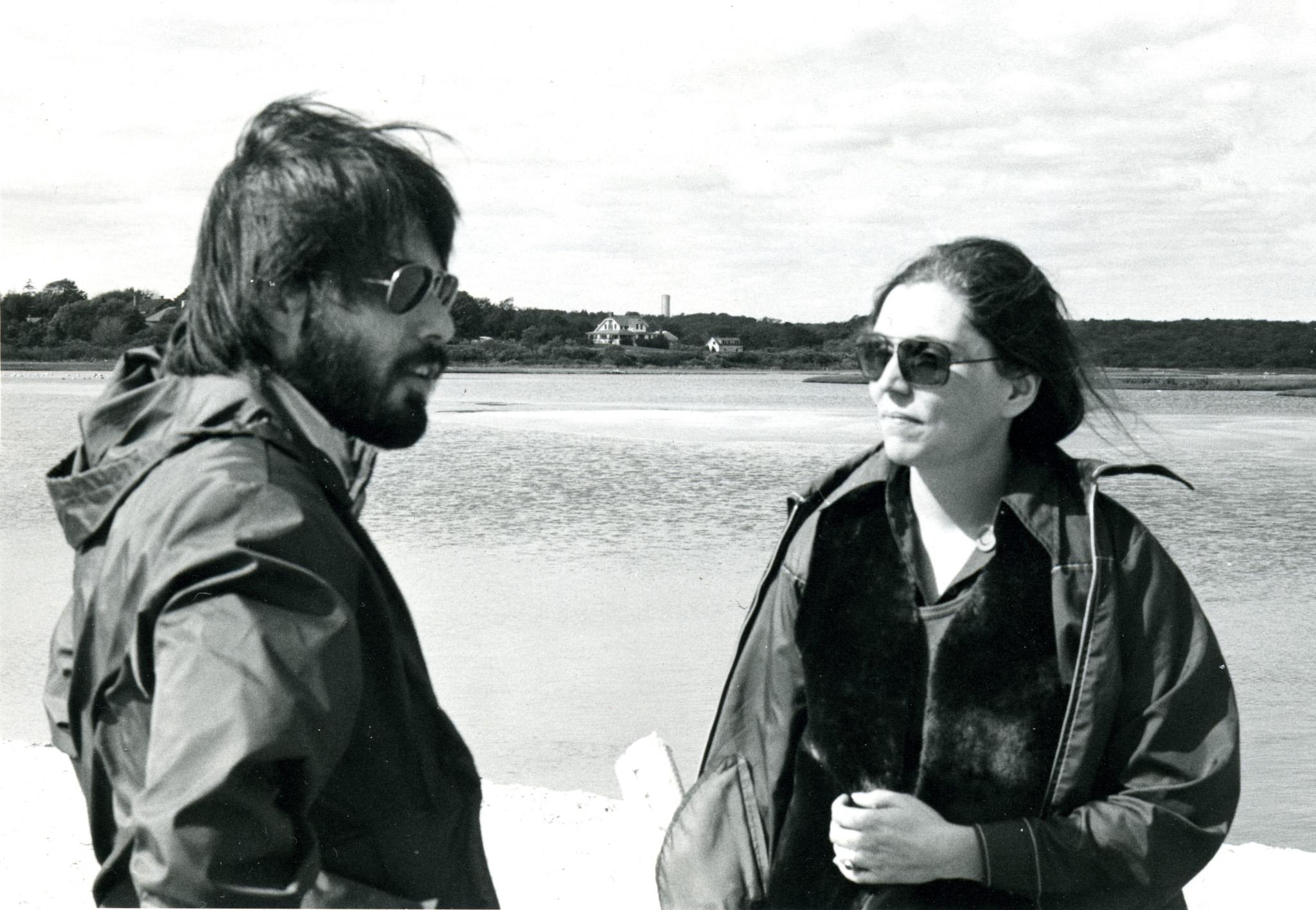 two people stand conversing on a shoreline