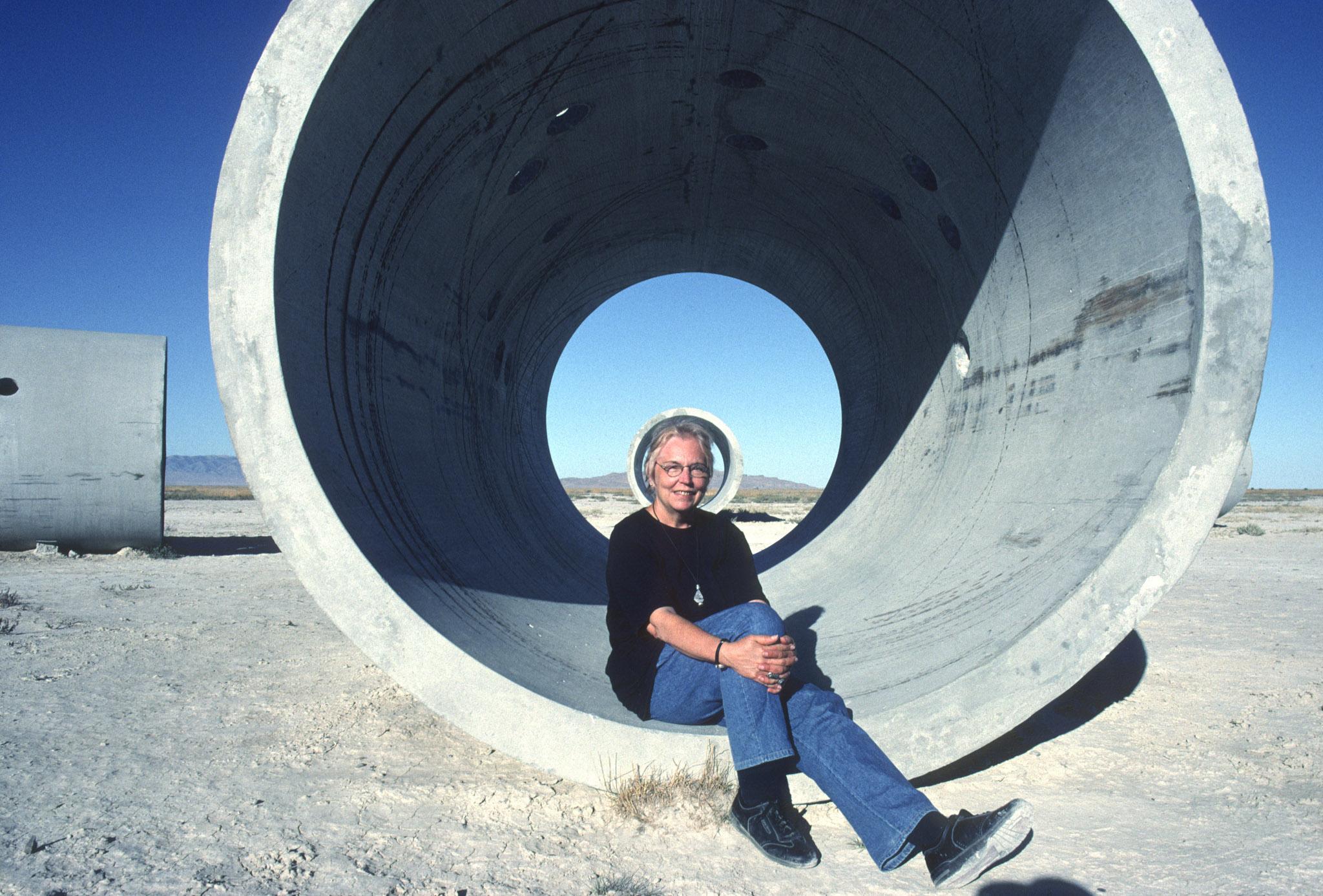 Nancy Holt sitting inside one tunnel of Sun Tunnels 