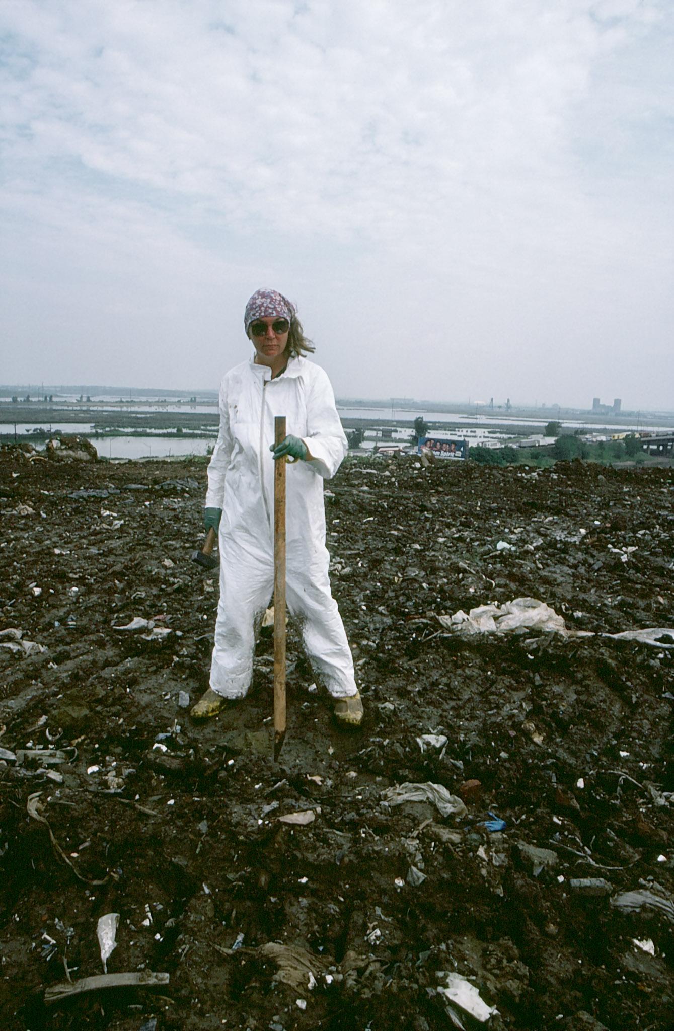 Nancy Holt standing in a landfill wearing a white full body suit
