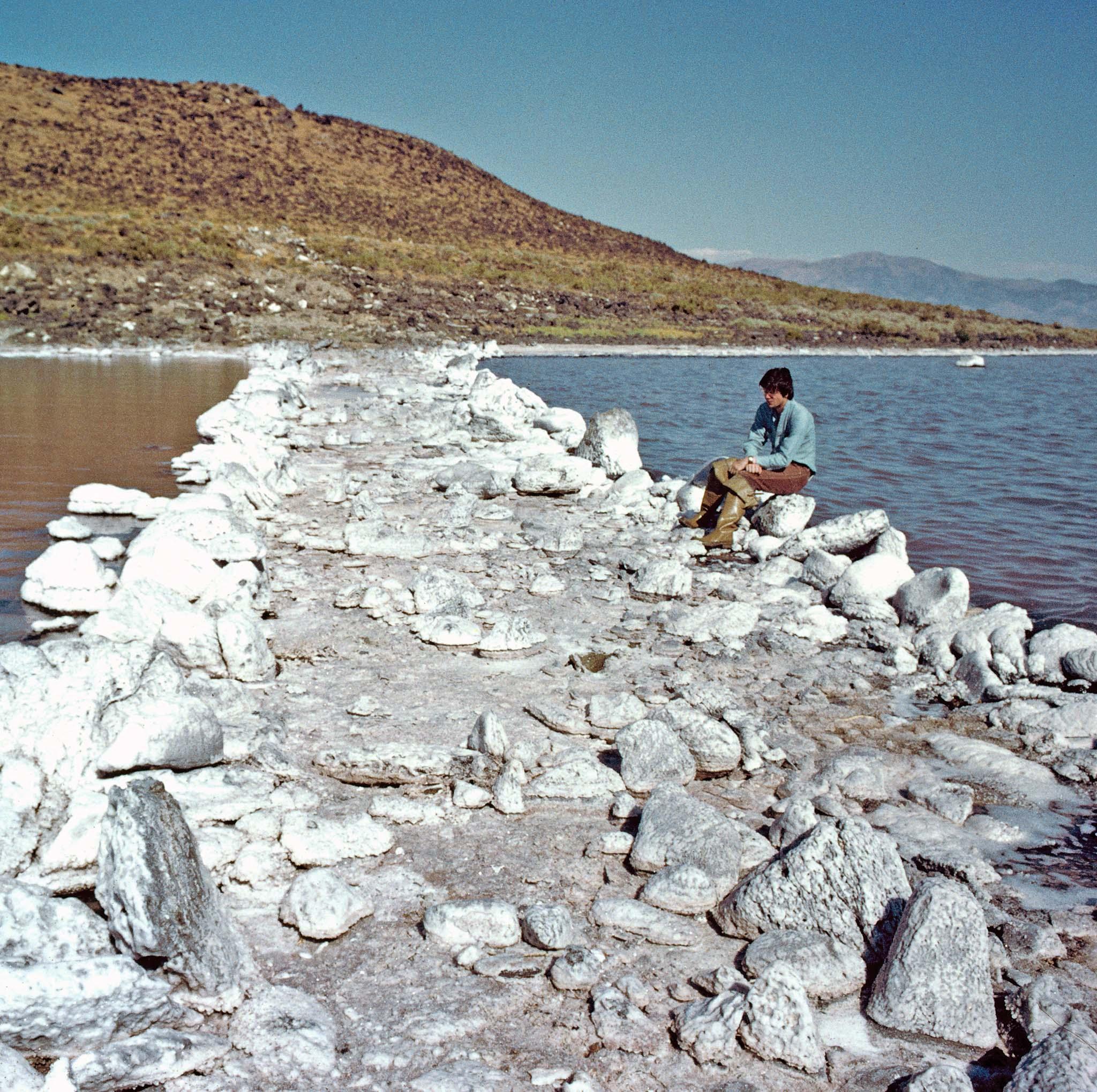 Robert Smithson seated at the edge of a salt encrusted Spiral Jetty