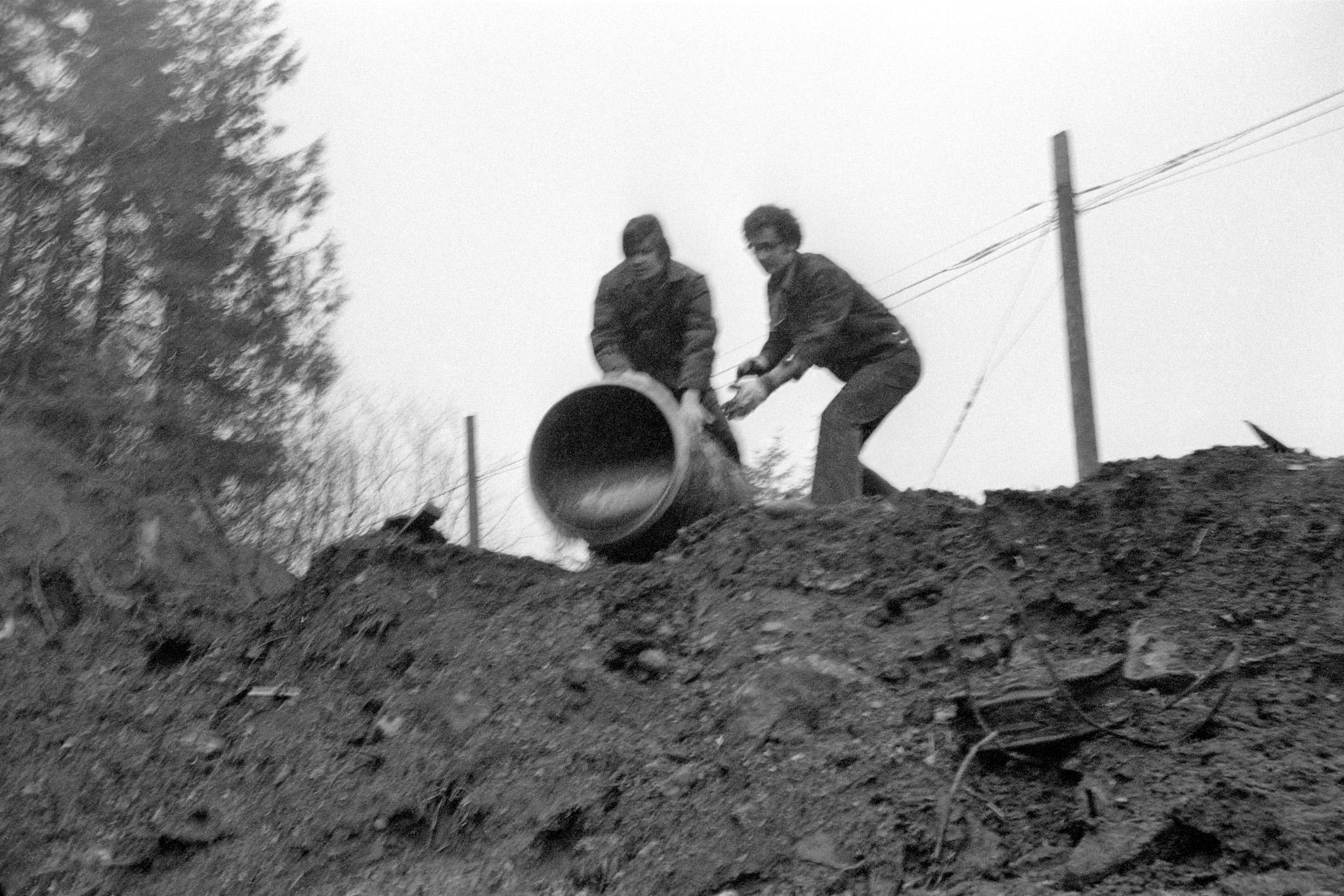 Robert Smithson and one other person pouring glue down a muddy hillside