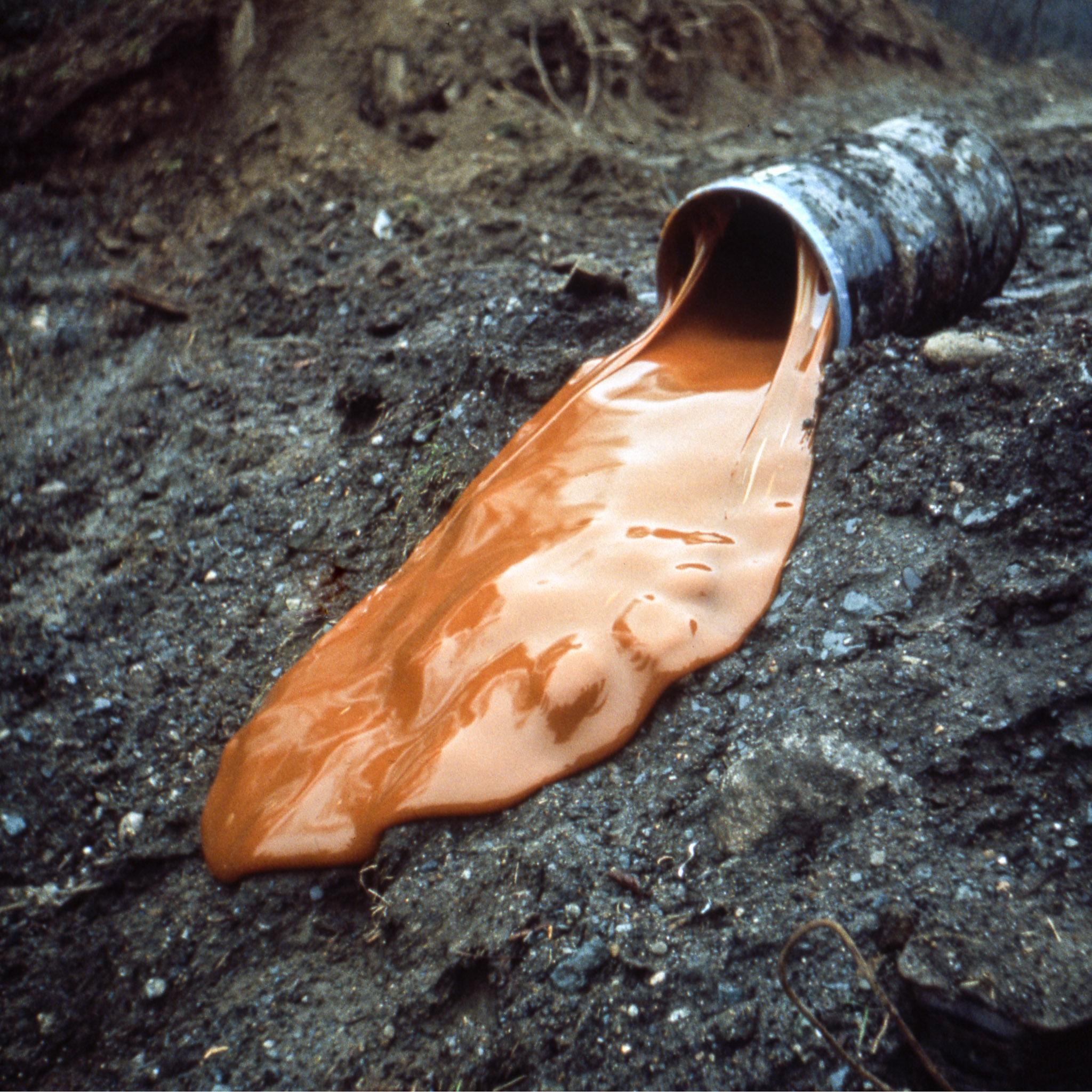 Viscous orange glue slowly pouring down a muddy hillside out of a large barrel
