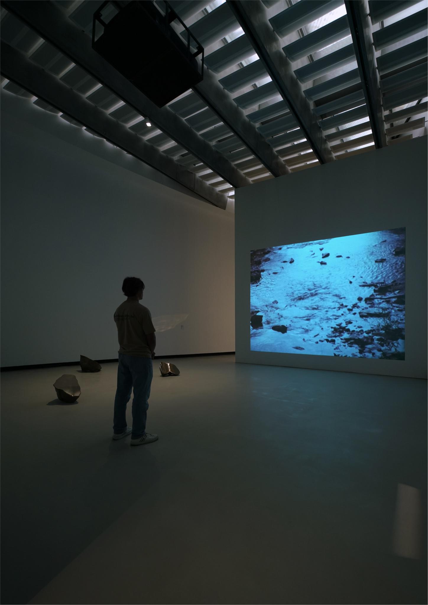 installation view of a tall museum gallery space with a projection of water on one wall
