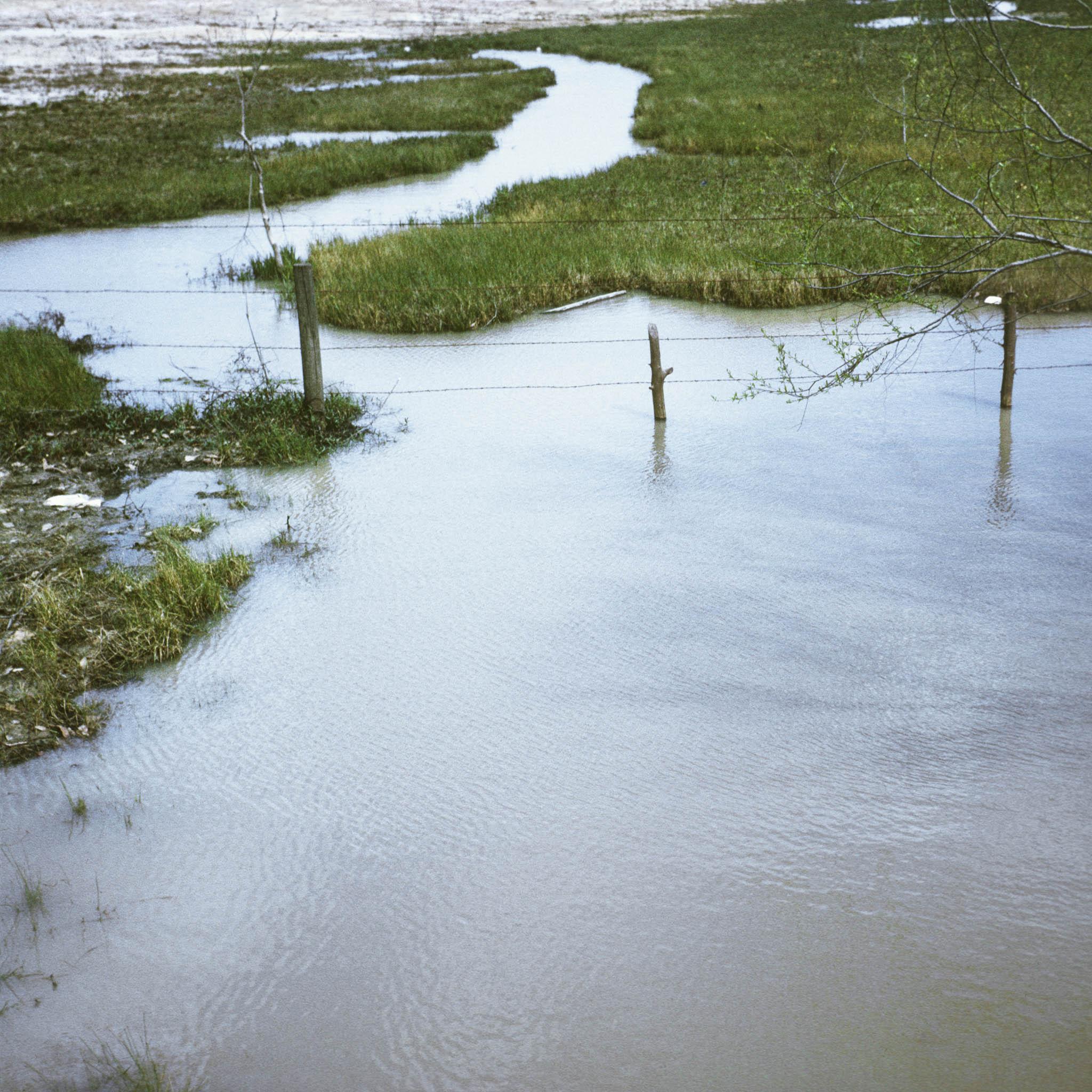 a flooded drainage with a barbed wire fence cutting through the water in a bucolic landscape