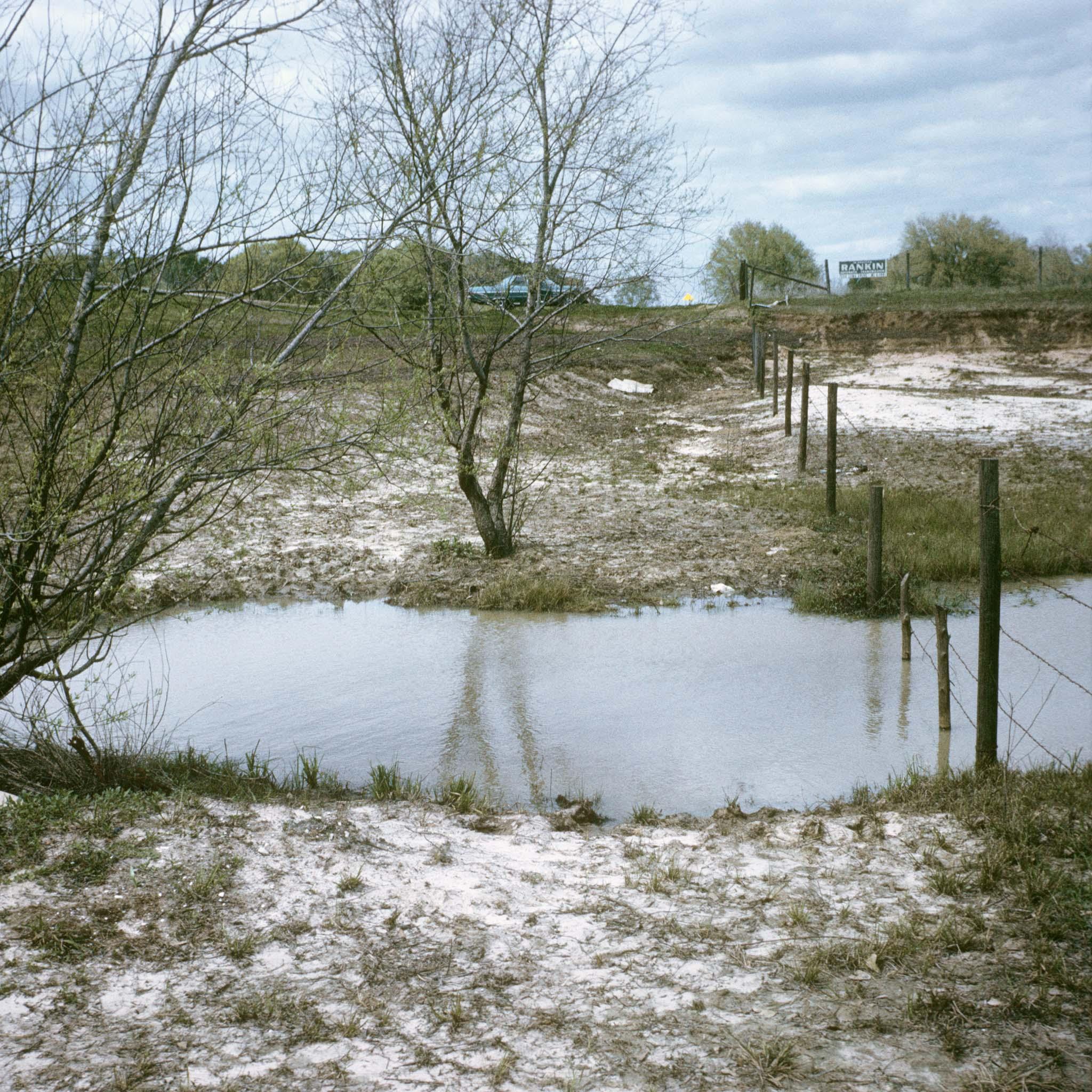 a flooded drainage with a barbed wire fence cutting through the water in a bucolic landscape