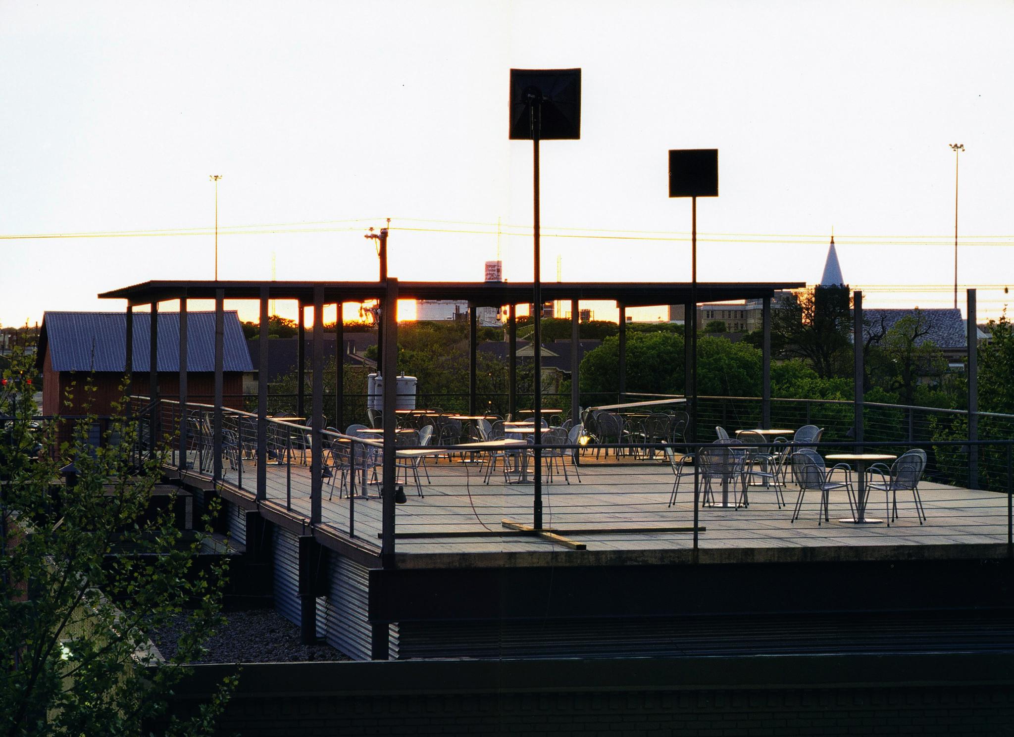 a large platform balcony at sunset, showing tables and chairs