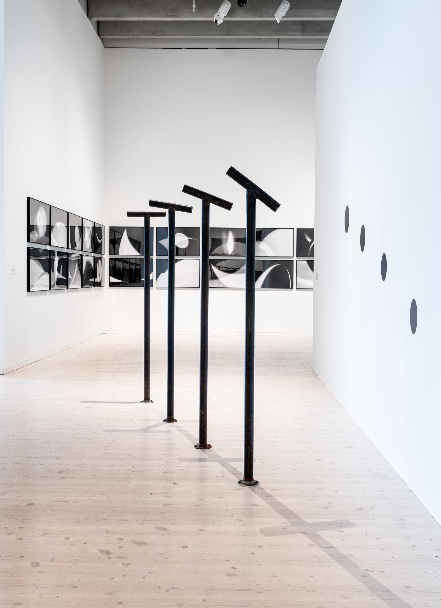 four steel pipes attached to the floor with viewing pipes attached to the top, each looking at a painted black circle on a wall