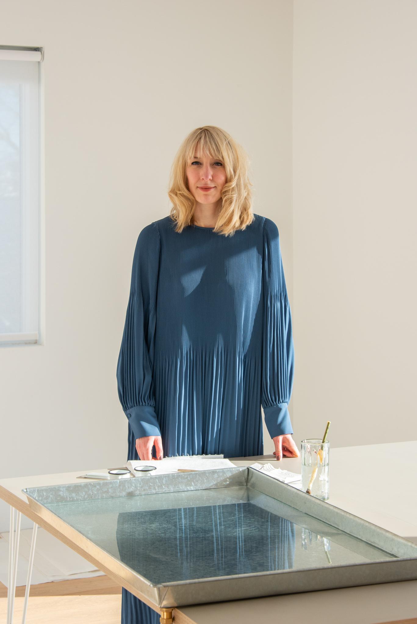 a woman wearing a blue dress standing in an art studio