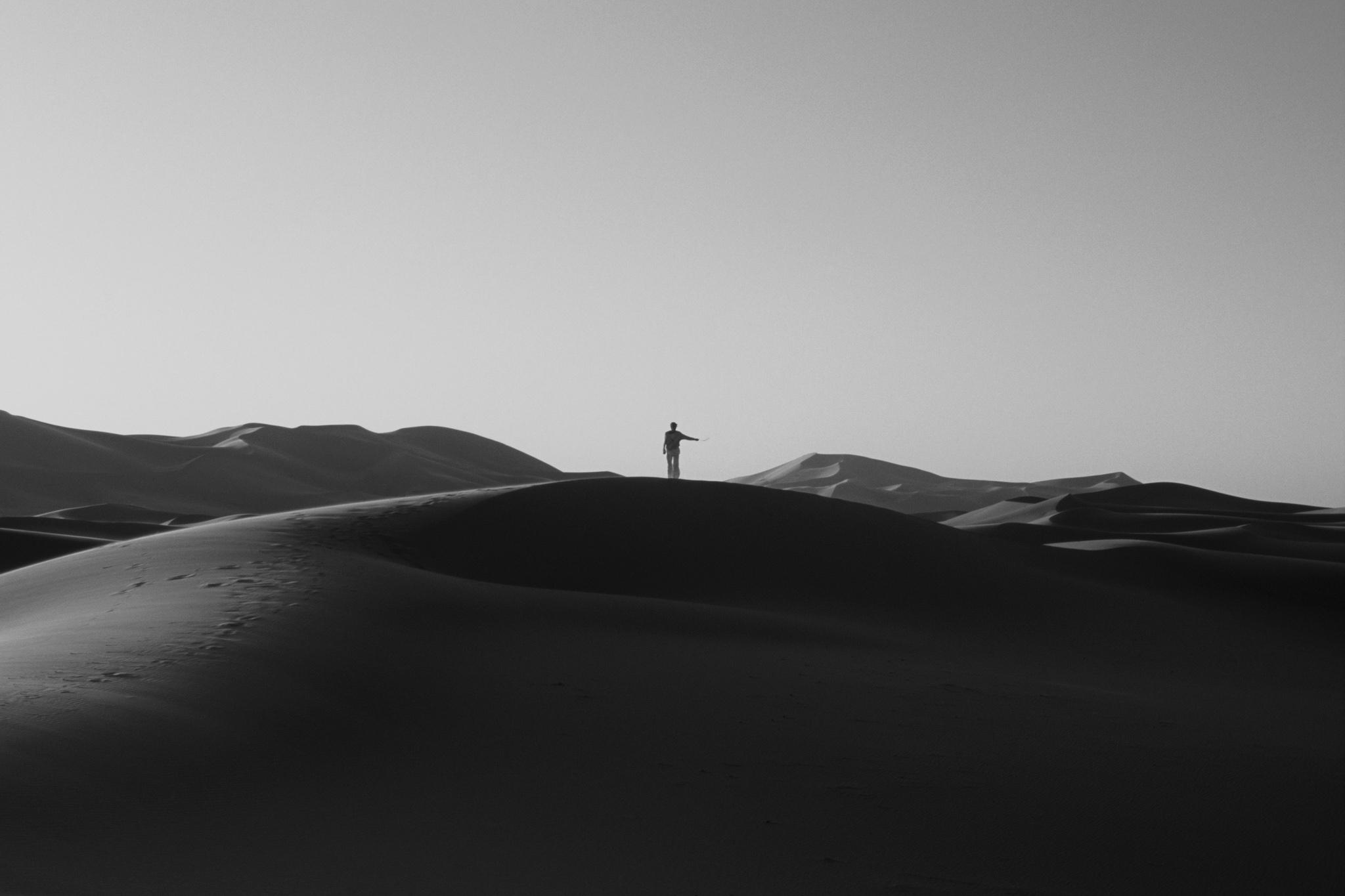 a large desert dune with a figure standing with an outstretched arm in the center horizon